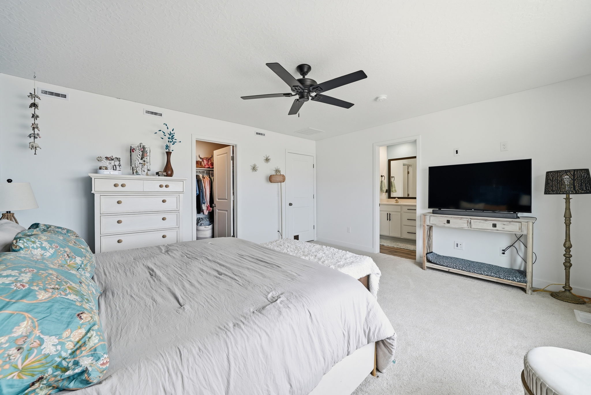 Spacious bedroom featuring light-colored carpeting, a black ceiling fan, and white walls