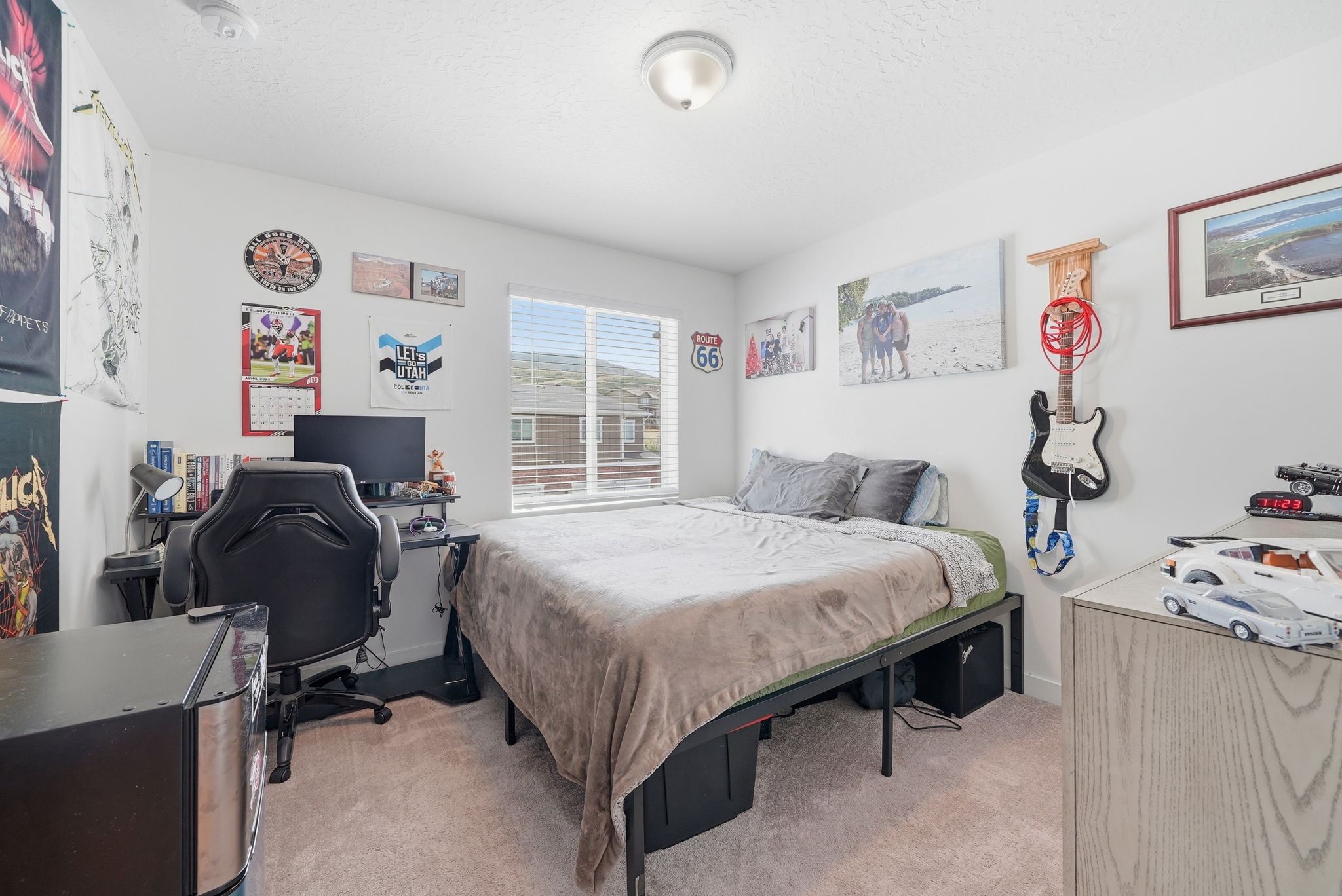 Bright bedroom featuring a large window with blinds, neutral carpeting, and a ceiling-mounted light fixture