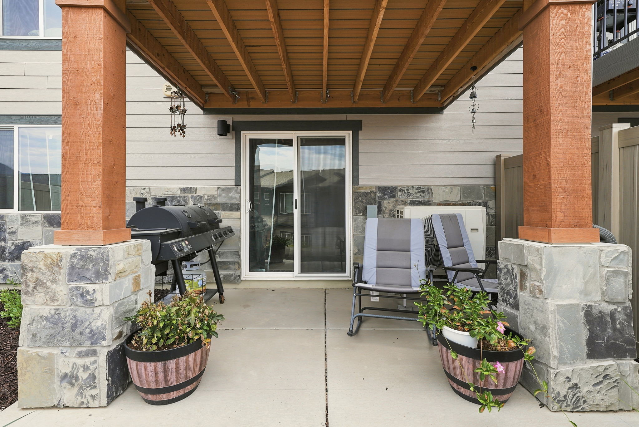 Covered patio featuring concrete flooring, stone-clad pillars, a wood-finish ceiling, and a sliding glass door