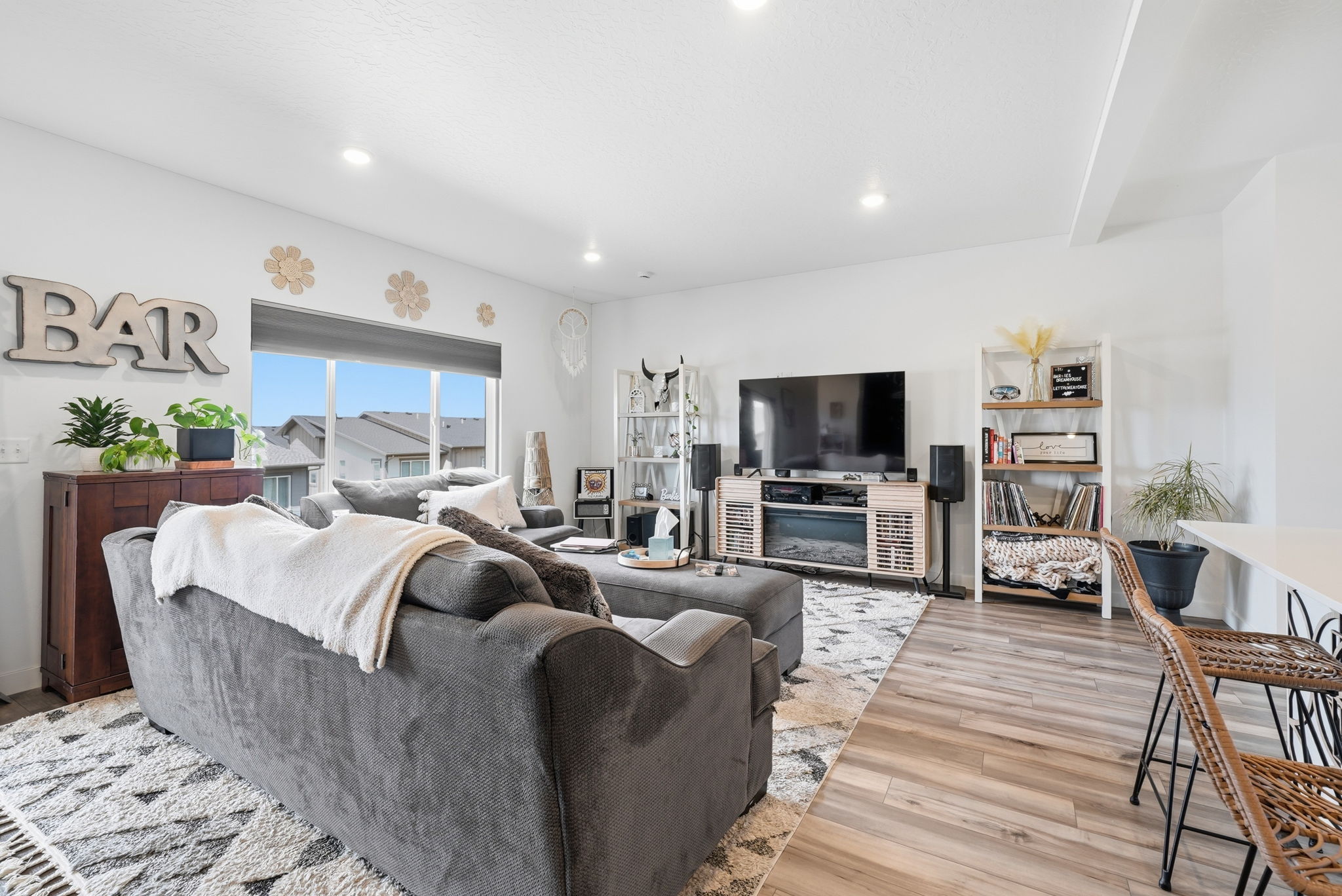 Open-concept living area featuring light wood-finish flooring, recessed lighting, a built-in media console with a fireplace, and a large window