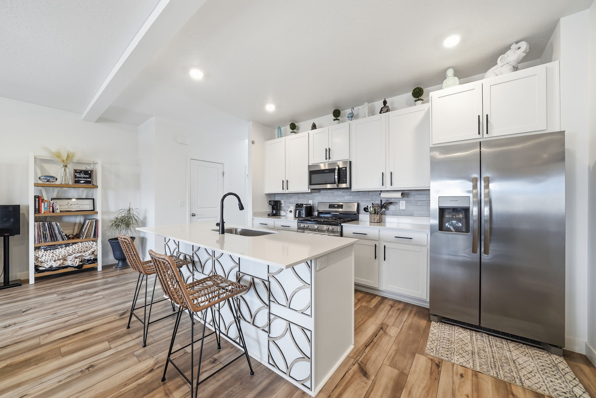 Open-concept kitchen featuring an island with decorative tile detailing, white cabinetry, stainless steel appliances, and wood-finish flooring