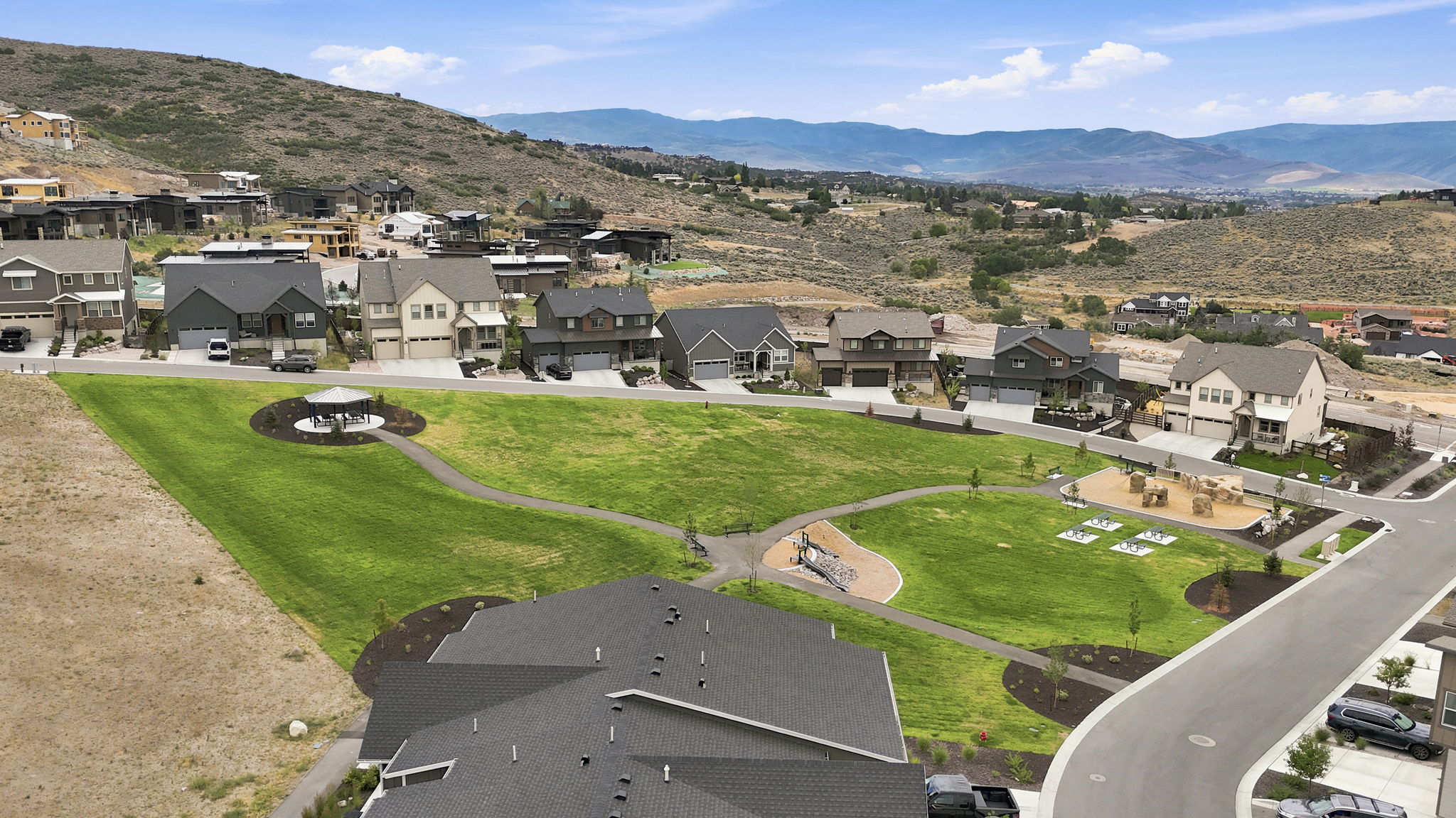 Expansive green space featuring a paved walking path, a circular gazebo, and recreational equipment