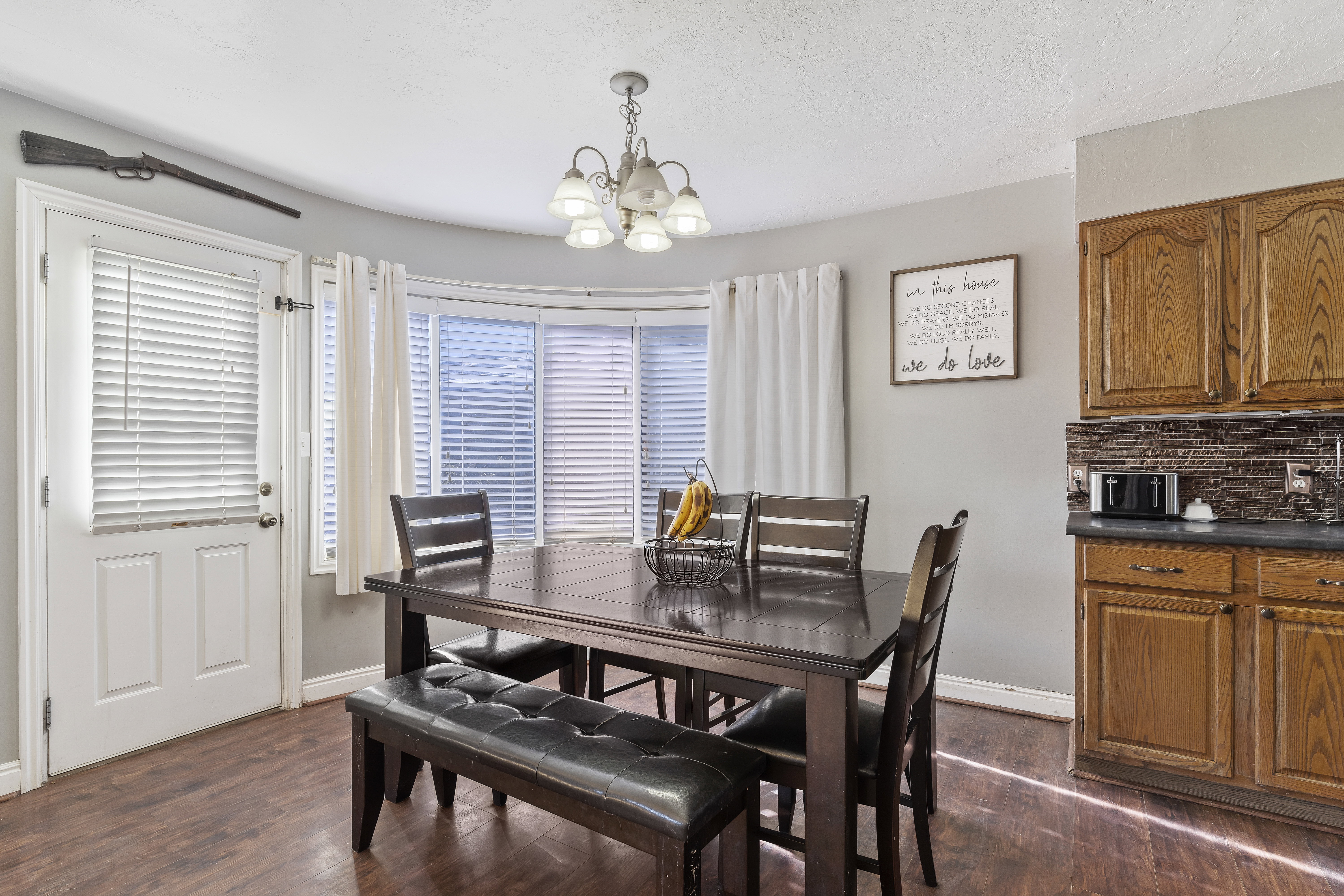 Dining area featuring wood-finish flooring, a bay window with blinds, and a built-in kitchen cabinet with a tile backsplash