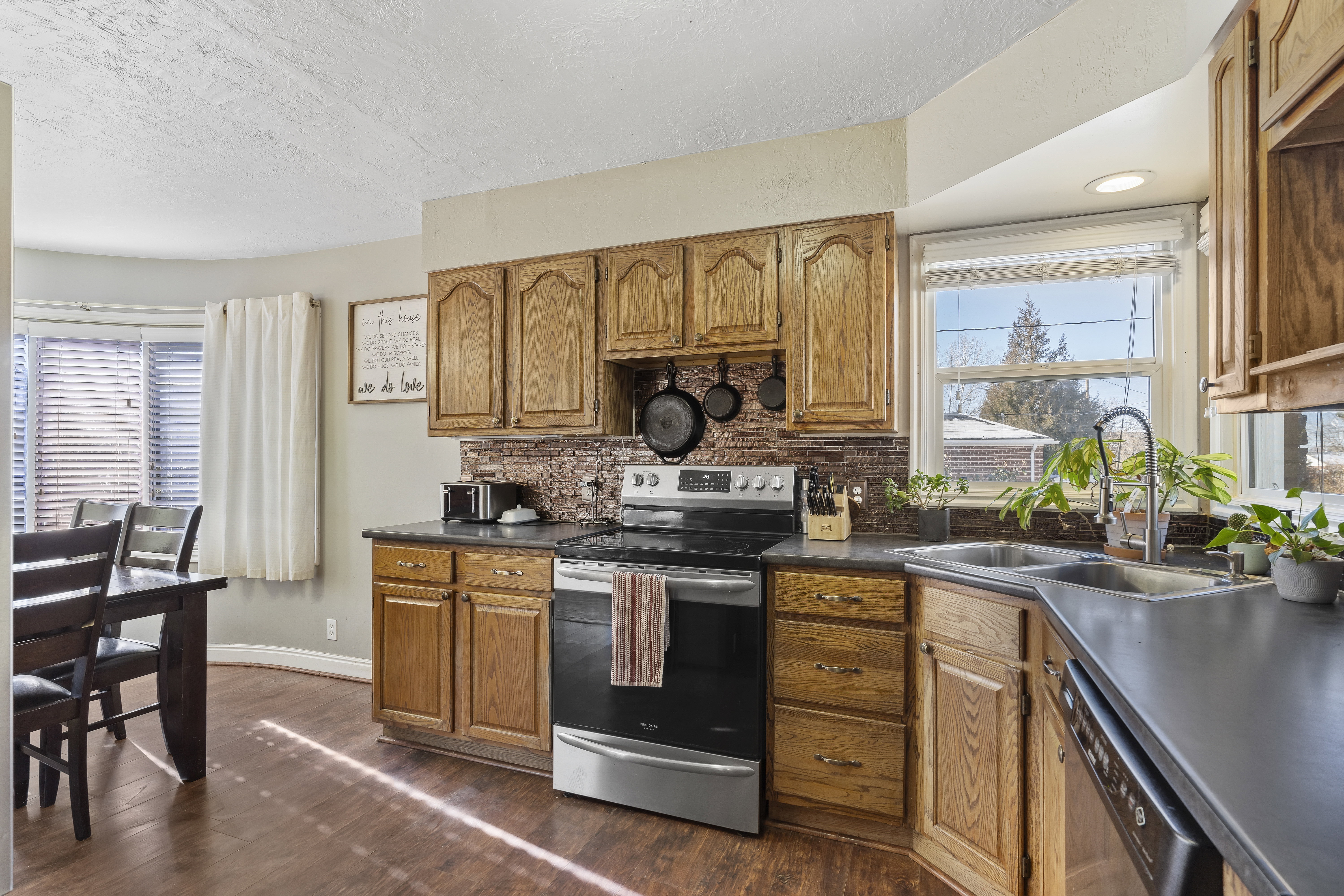 Kitchen featuring wood-finish flooring, oak cabinetry, dark countertops, a mosaic tile backsplash, and a stainless steel oven/range