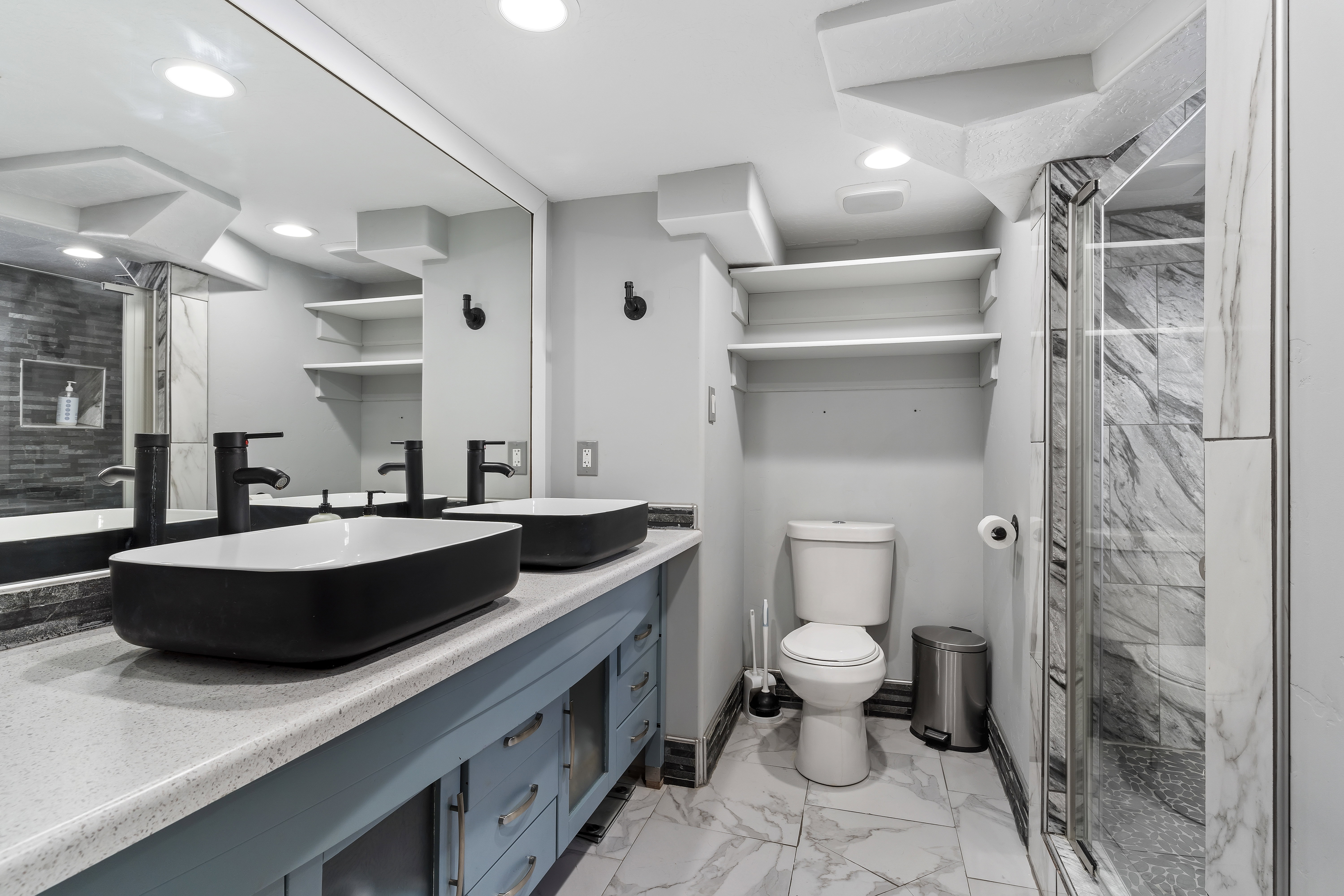 Contemporary bathroom featuring a double vanity with vessel sinks, light-toned countertop, and blue cabinetry
