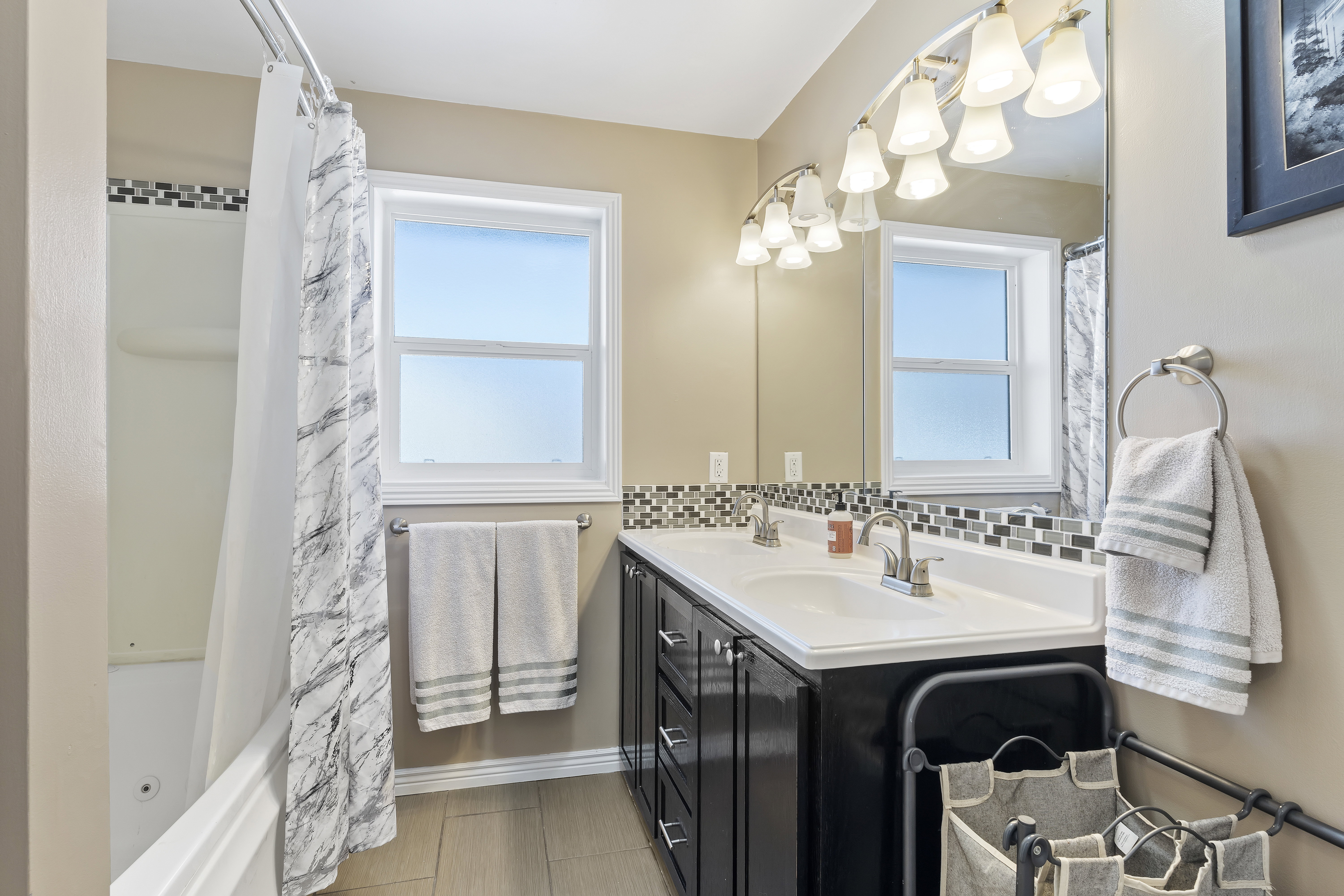Bathroom featuring a double vanity with two sinks, dark cabinetry, and a full-width mirror