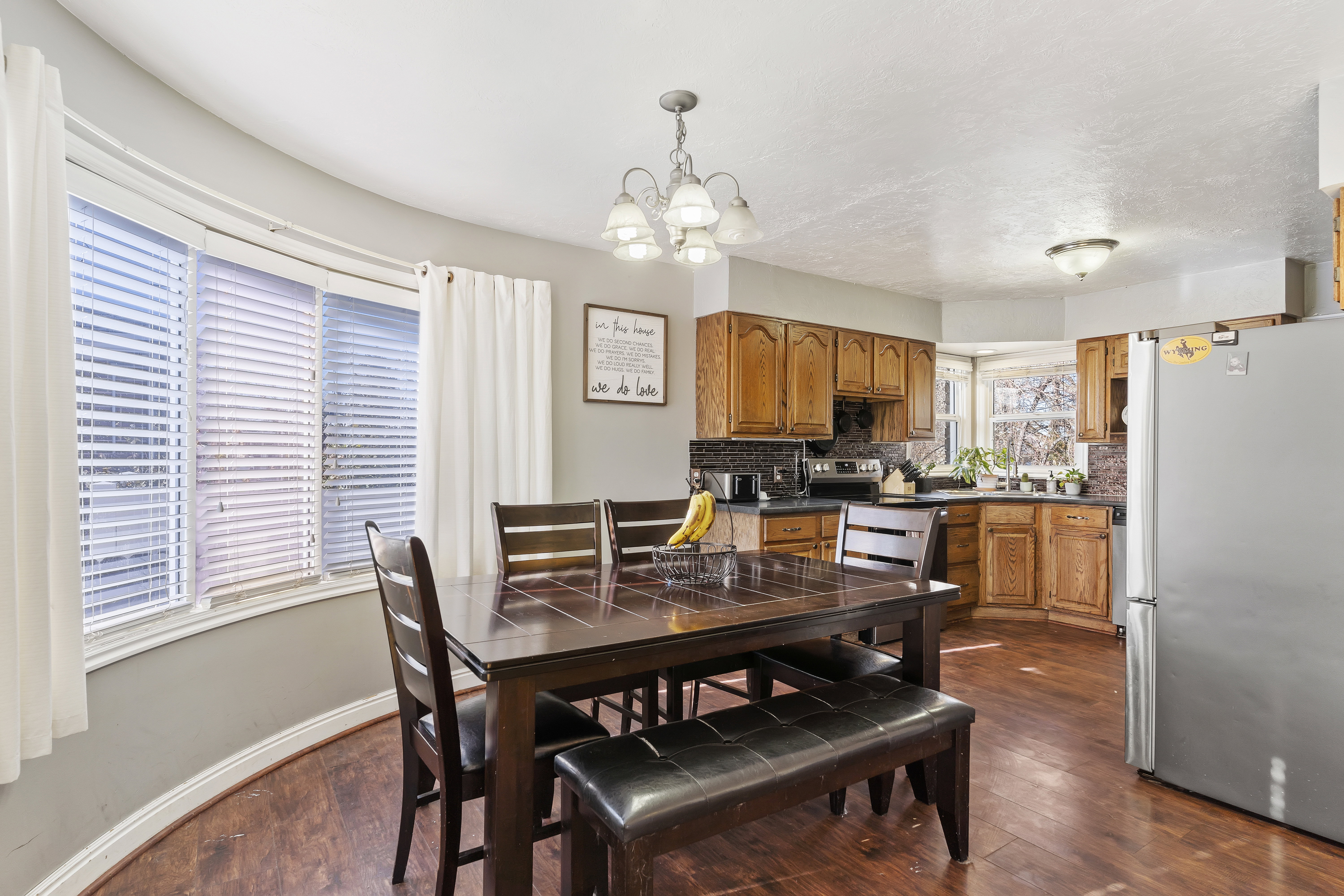 Dining area featuring a curved bay window with blinds, wood-finish flooring, and a chandelier-style ceiling fixture