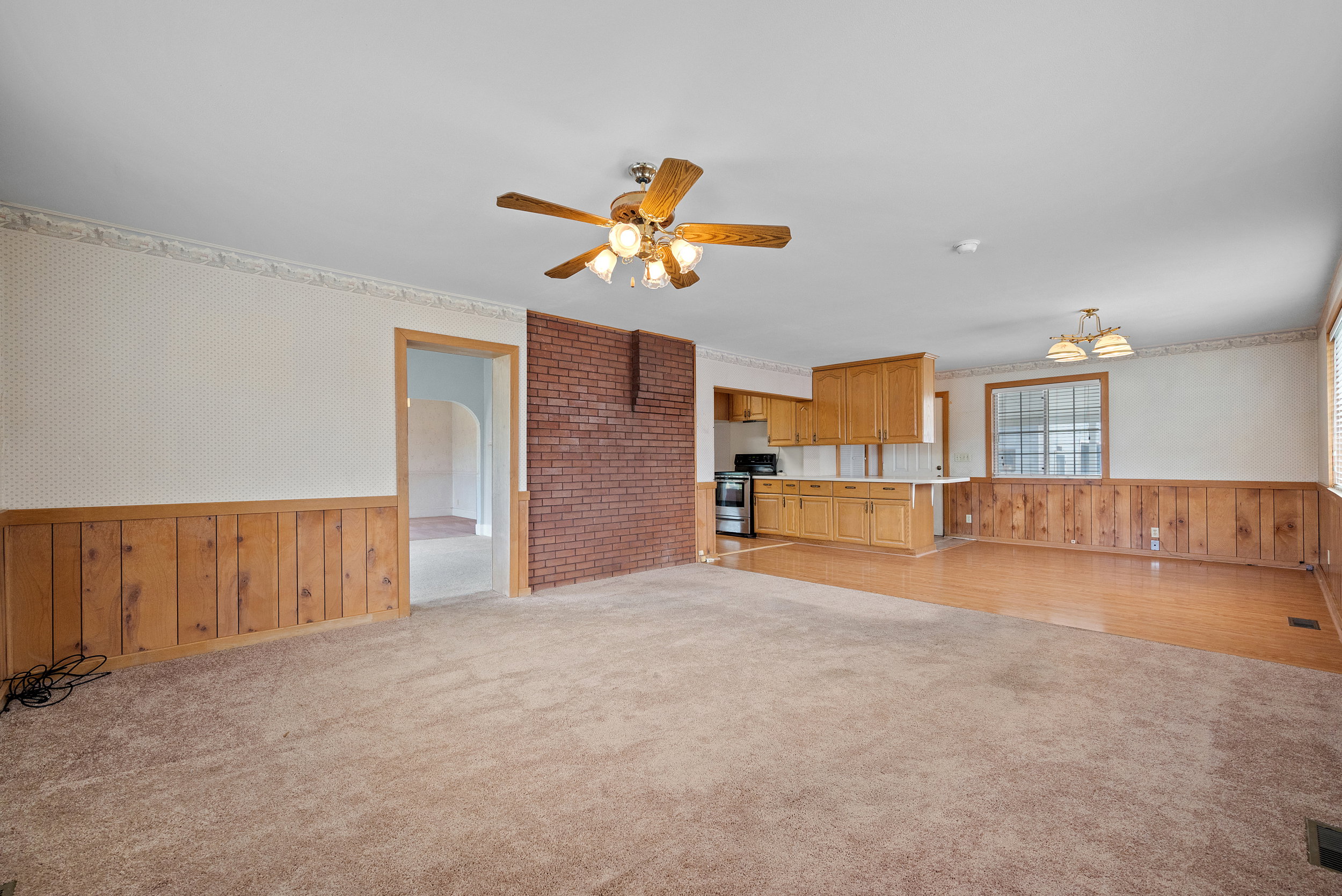 Open-concept living area featuring a brick accent wall, a ceiling fan with integrated lighting, and a combination of carpet and wood-finish flooring