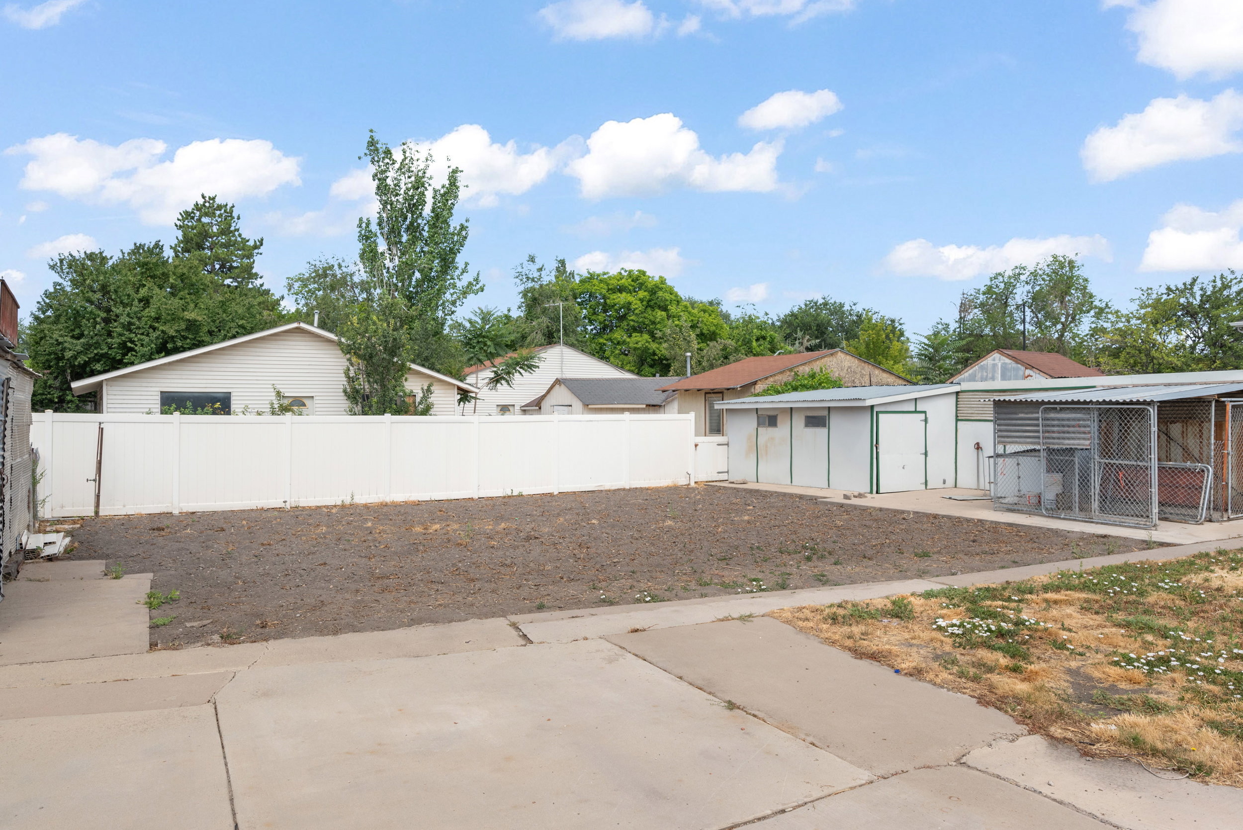Expansive outdoor space featuring a paved drive, a white privacy fence, and multiple outbuildings and designated garden area.