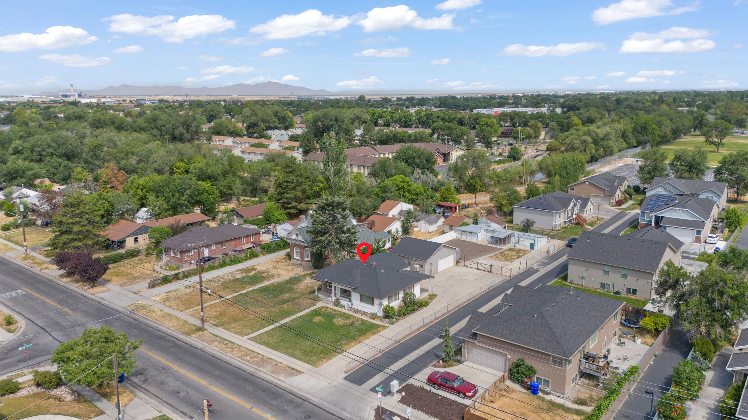 Aerial perspective showcasing a residential property with a dark shingle roof and light-colored siding, positioned on a corner lot with a green lawn