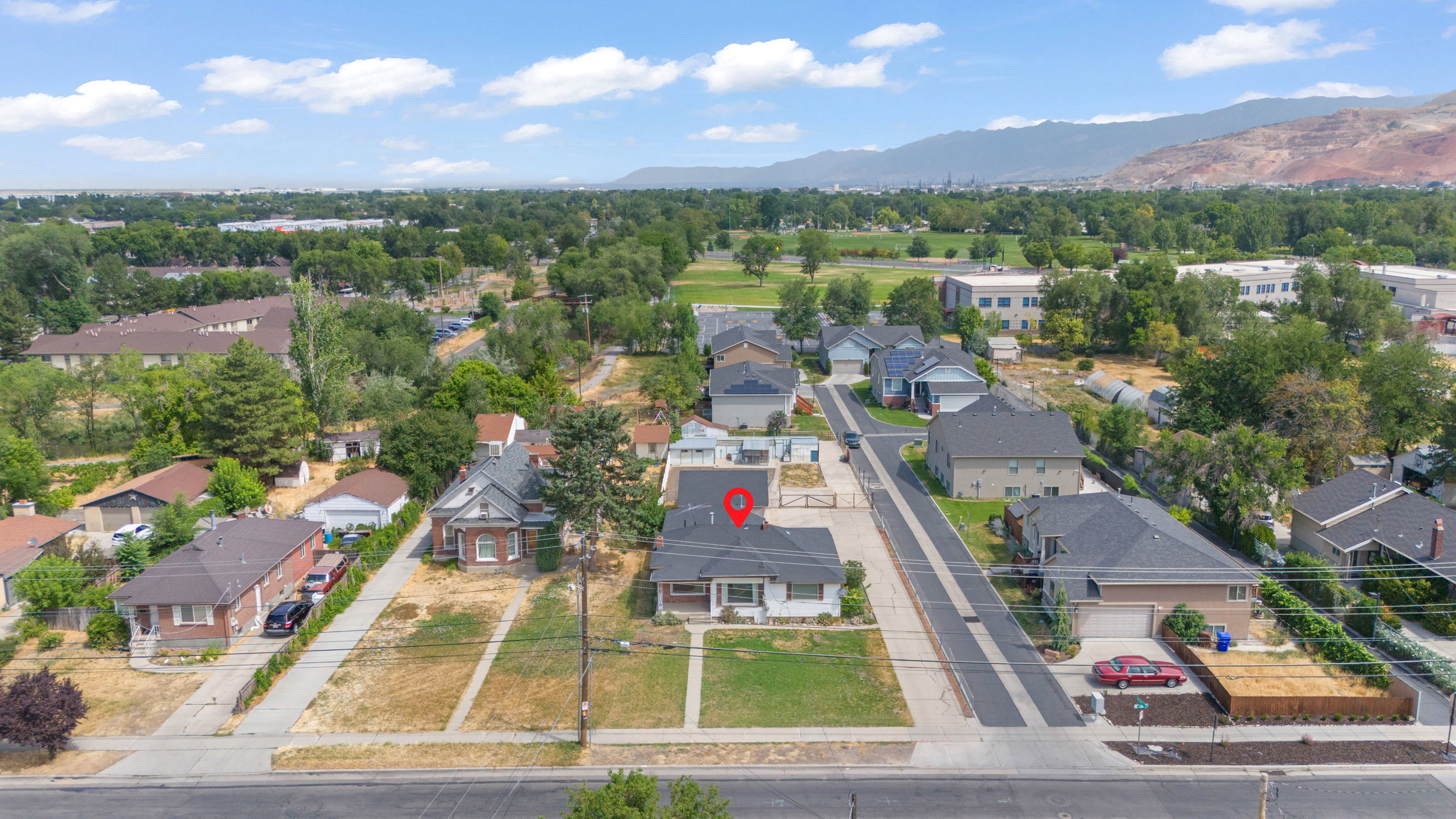 Aerial perspective showcasing a residential street with diverse architectural styles, mountain backdrop, and expansive green spaces