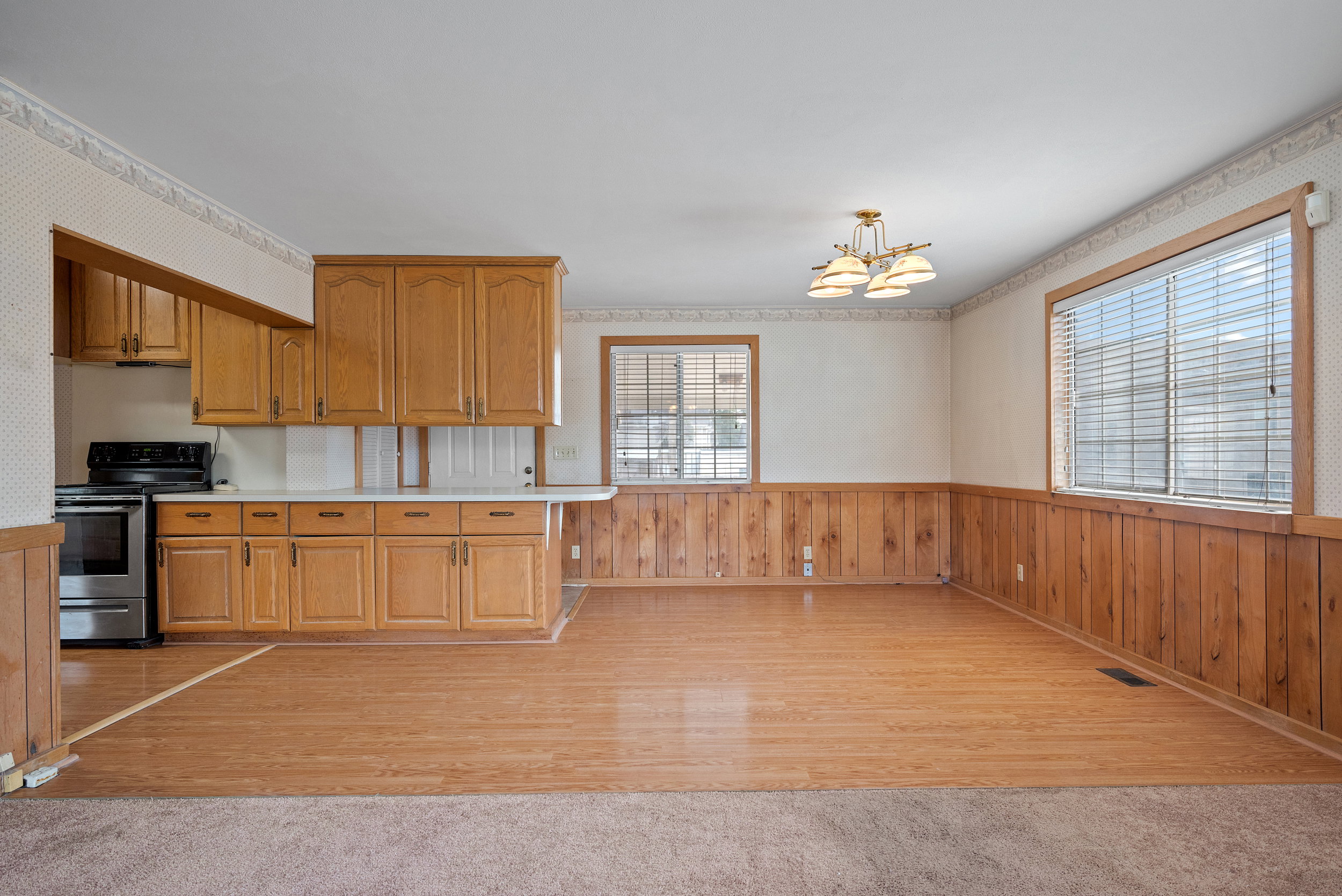 Kitchen and dining area featuring open concept living, wood-finish flooring, wood paneling, a stainless steel range, light wood cabinetry, and a chandelier