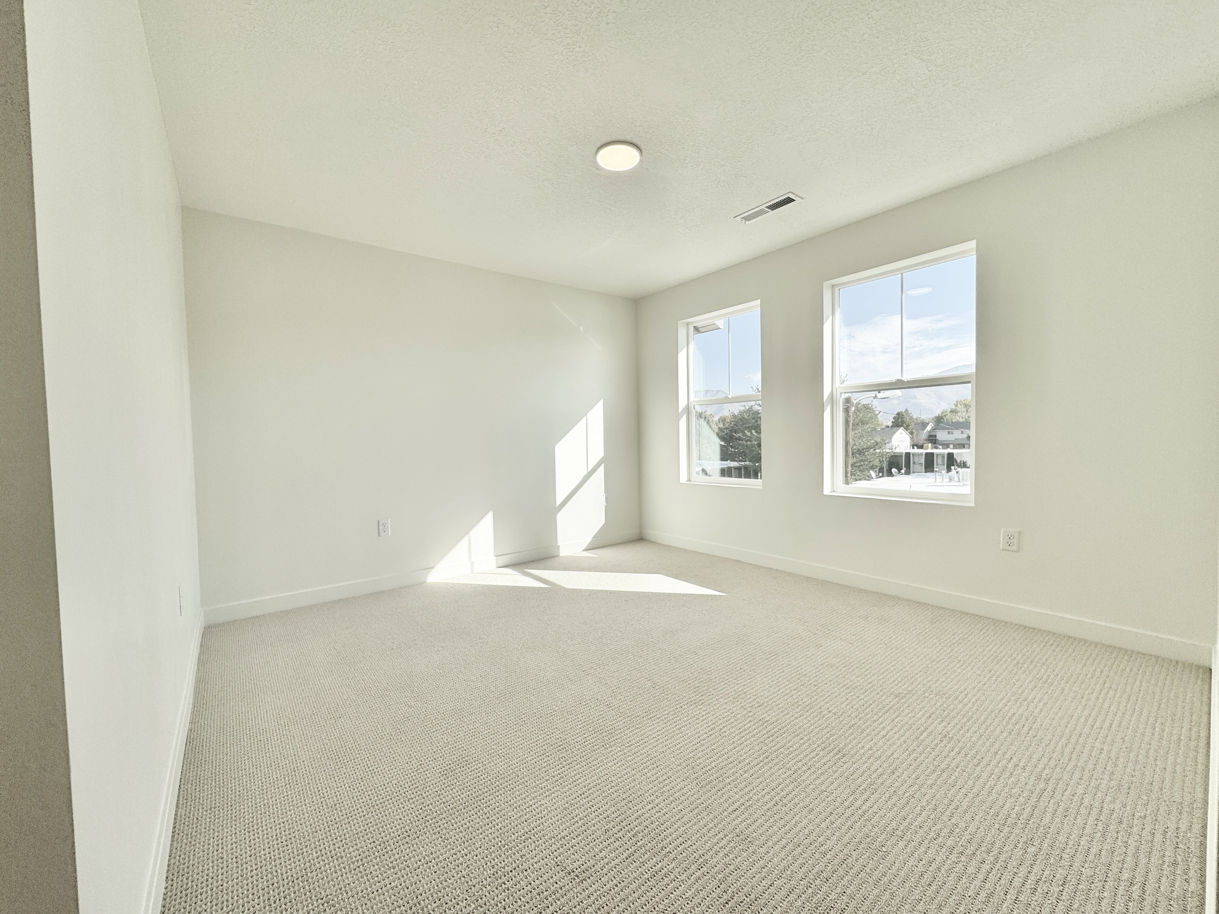Light-filled room featuring two windows, neutral tone carpeting, white walls, and recessed lighting