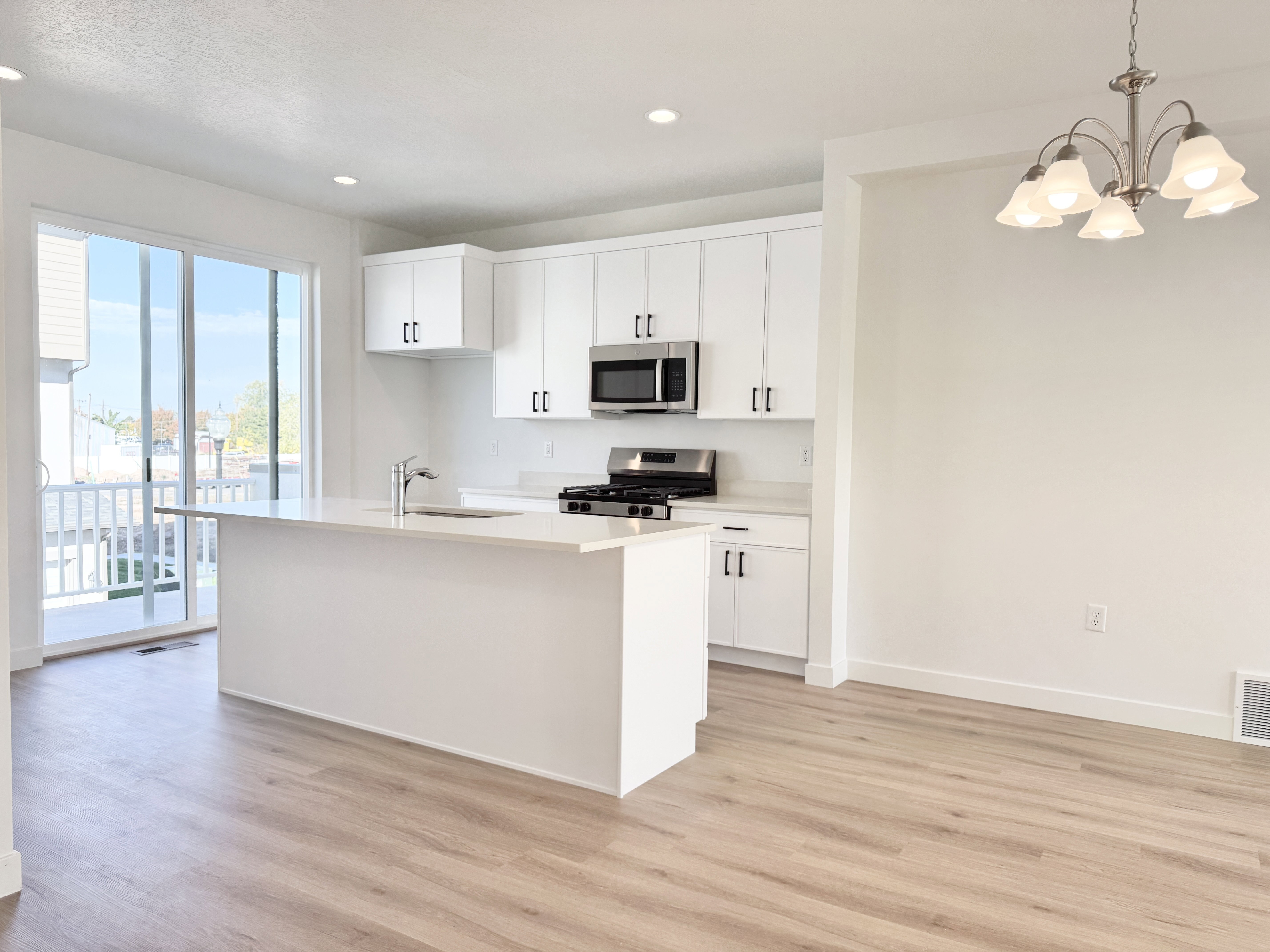 Contemporary kitchen featuring white cabinetry, stainless steel appliances, a center island with sink, and wood-finish flooring