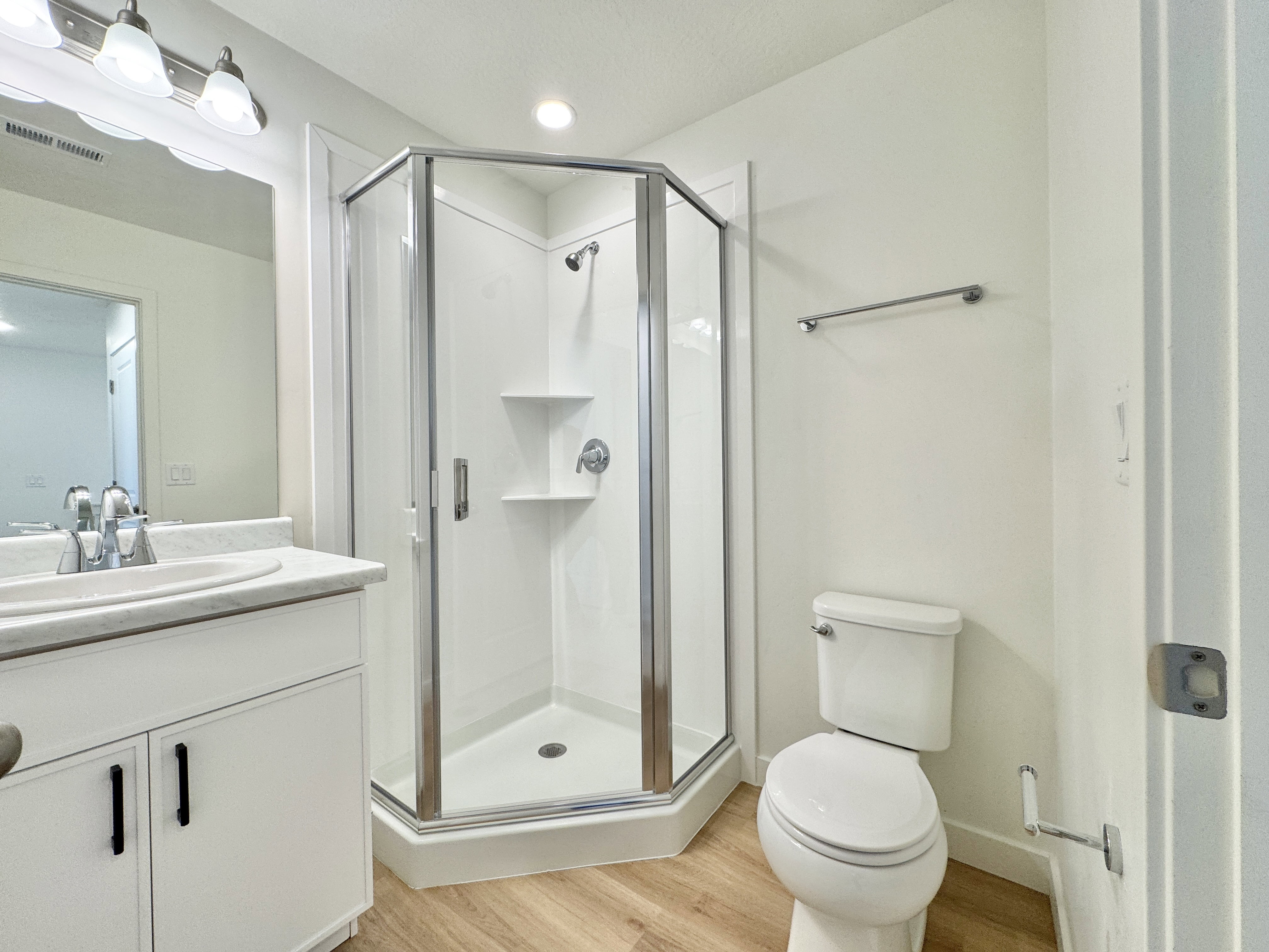 Corner glass-enclosed shower with integrated shelving, chrome fixtures, and a white base
