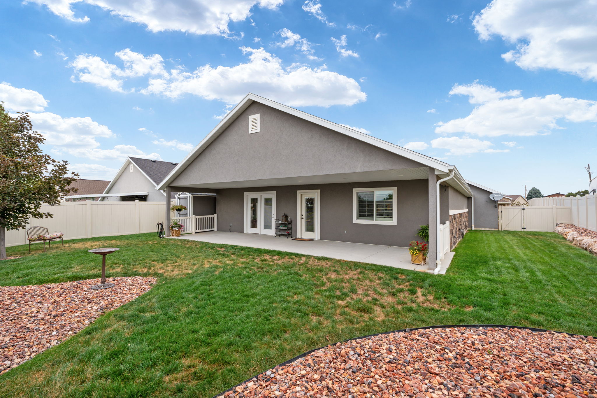 Expansive backyard featuring a covered patio, dual patio doors, manicured lawn, gravel landscaping, and a privacy fence