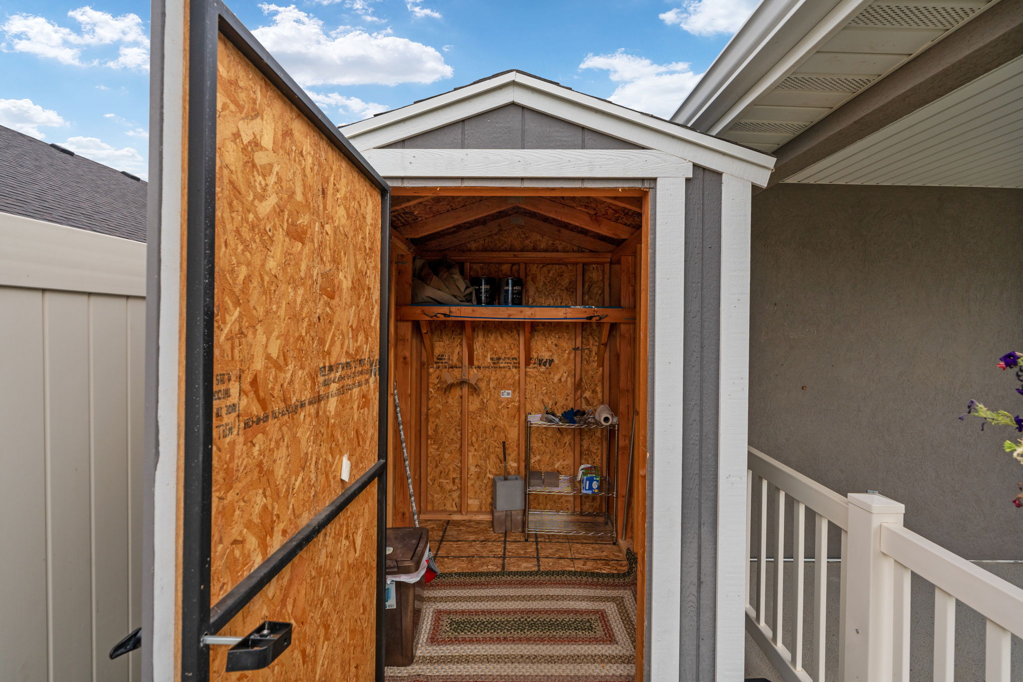 Utility shed featuring a gable roof, wood-finish interior walls, built-in shelving, and a patterned floor mat