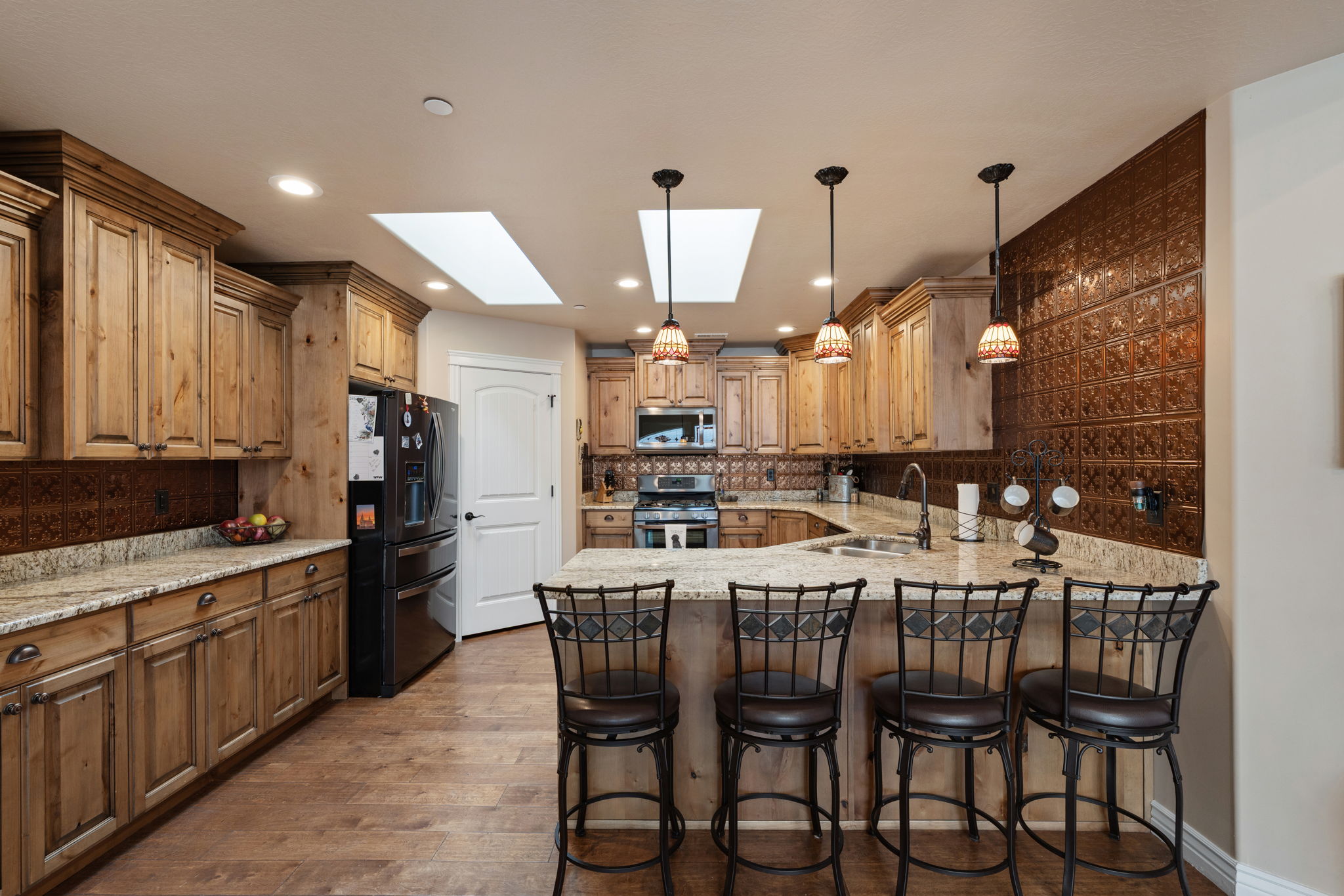 Kitchen featuring a large island with seating, natural wood cabinetry, granite countertops, and a full-height decorative backsplash