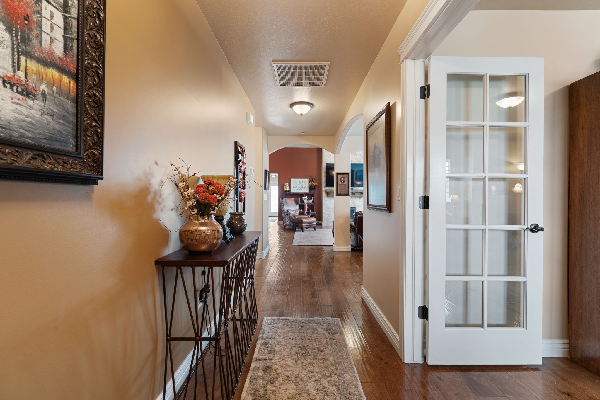 Hardwood flooring extends throughout this interior hallway, featuring a white French door with multiple glass panes