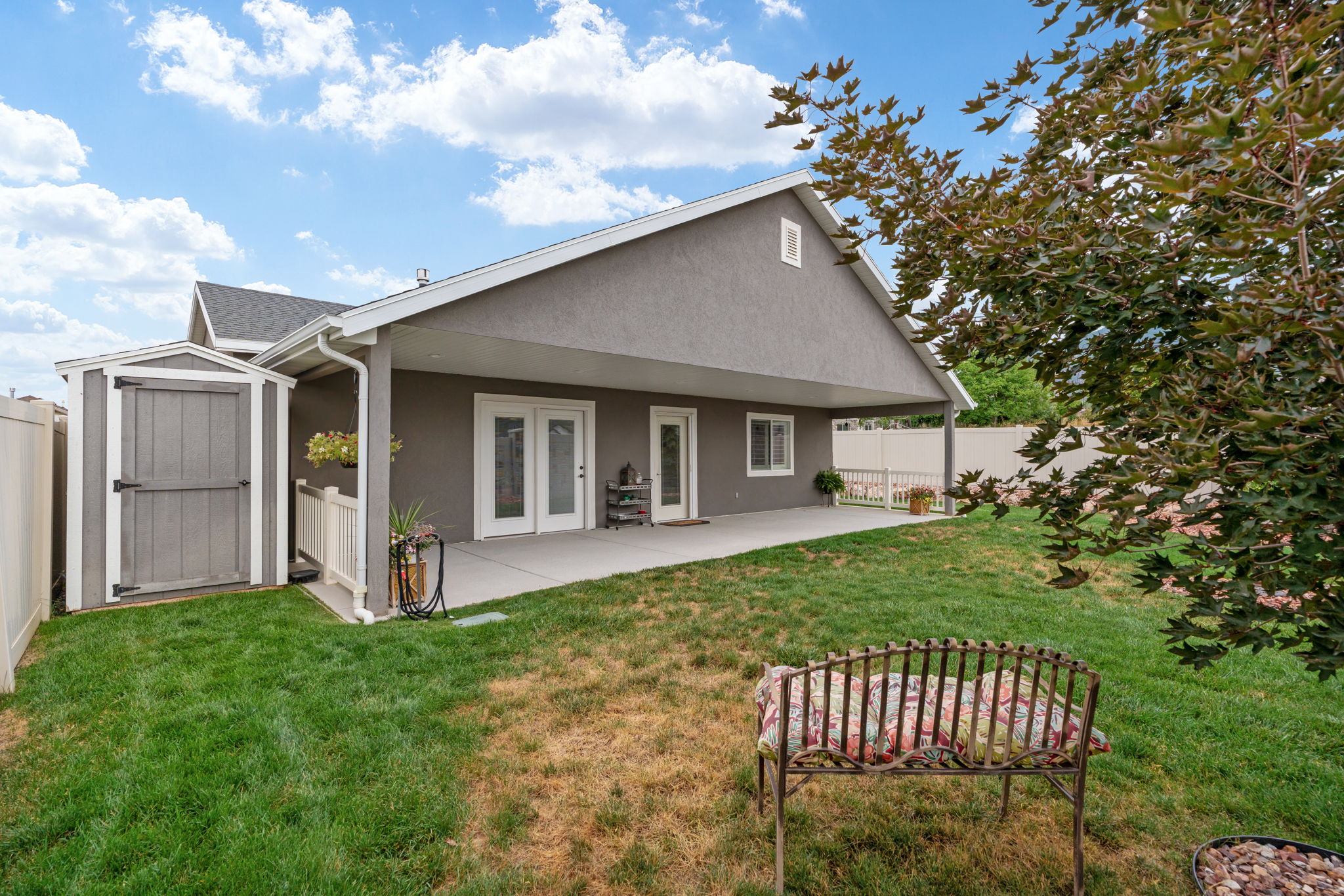 Expansive backyard featuring a covered patio, dual patio doors, a privacy fence, a detached shed, and a verdant lawn area