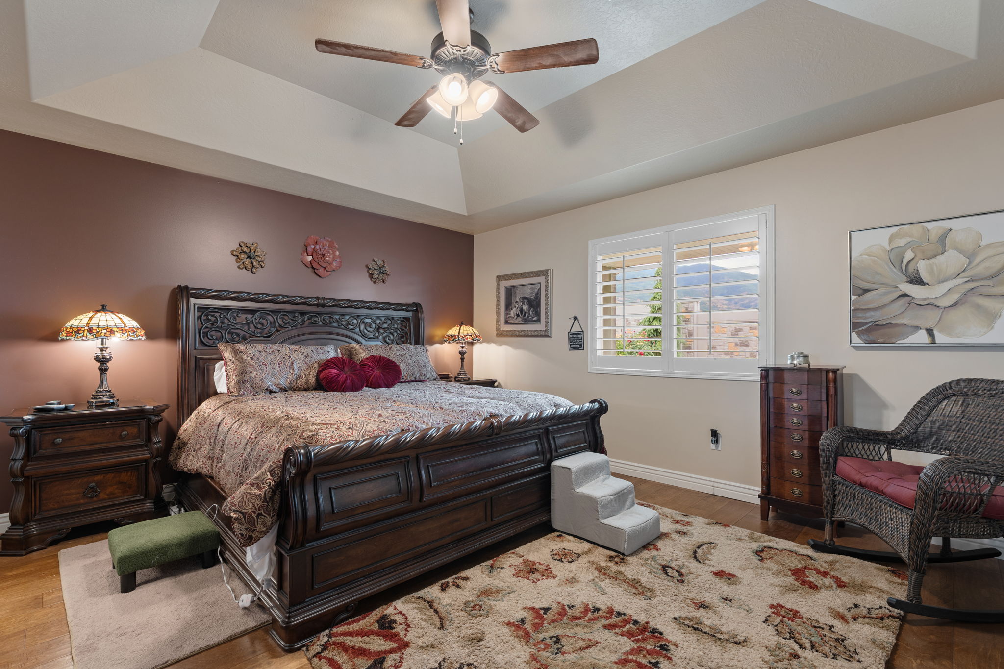 Bedroom featuring a tray ceiling with a ceiling fan, wood-finish flooring, and a window with plantation shutters