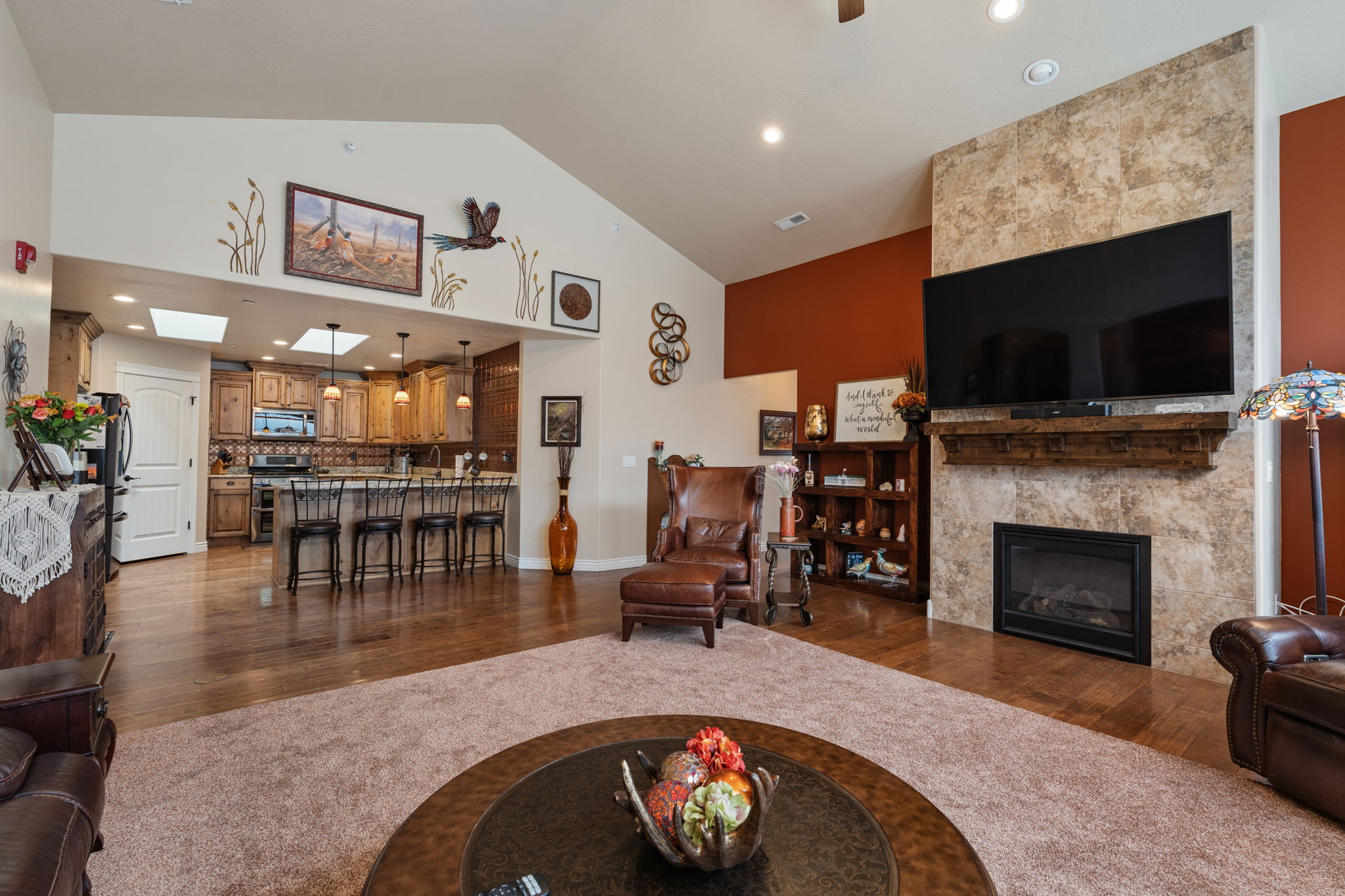 Vaulted ceiling living area featuring a stone-clad fireplace with a dark wood mantel, recessed lighting, and wood-finish flooring