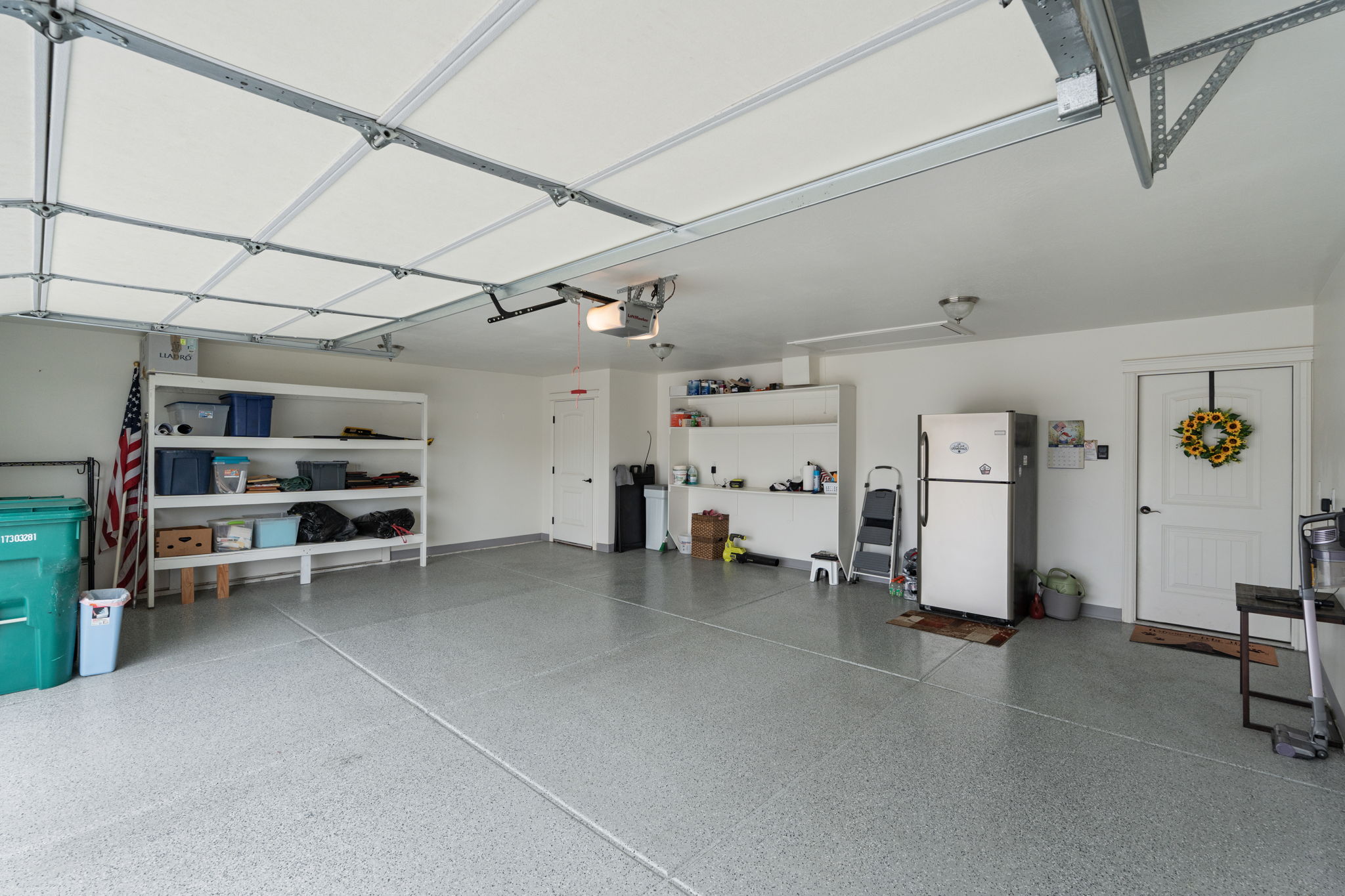 Spacious garage featuring a light gray epoxy floor coating, integrated overhead garage door, built-in shelving, and a secondary entry door