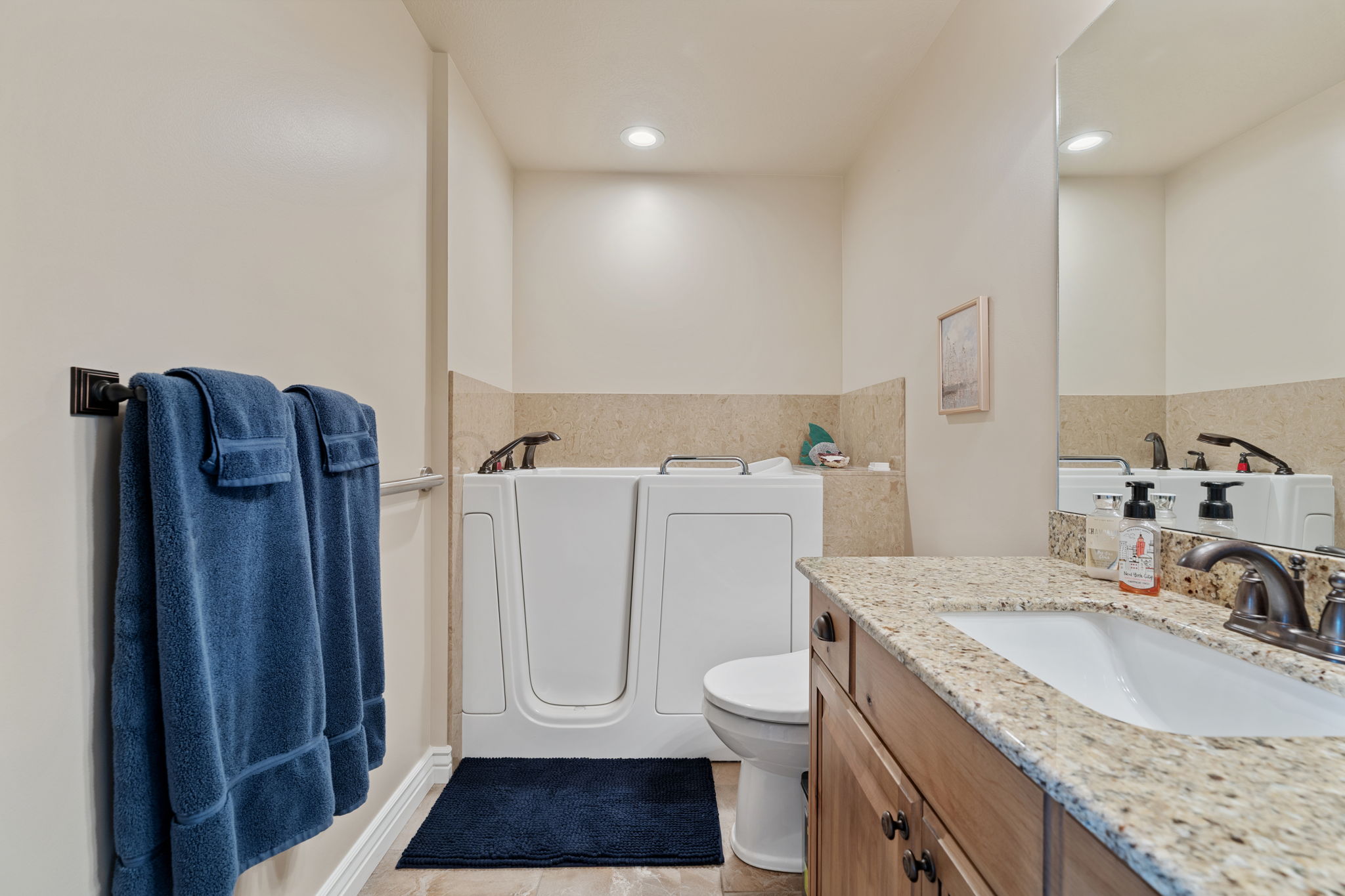 Bathroom featuring a walk-in tub, a vanity with a granite countertop, an undermount sink, and wood-finish cabinetry