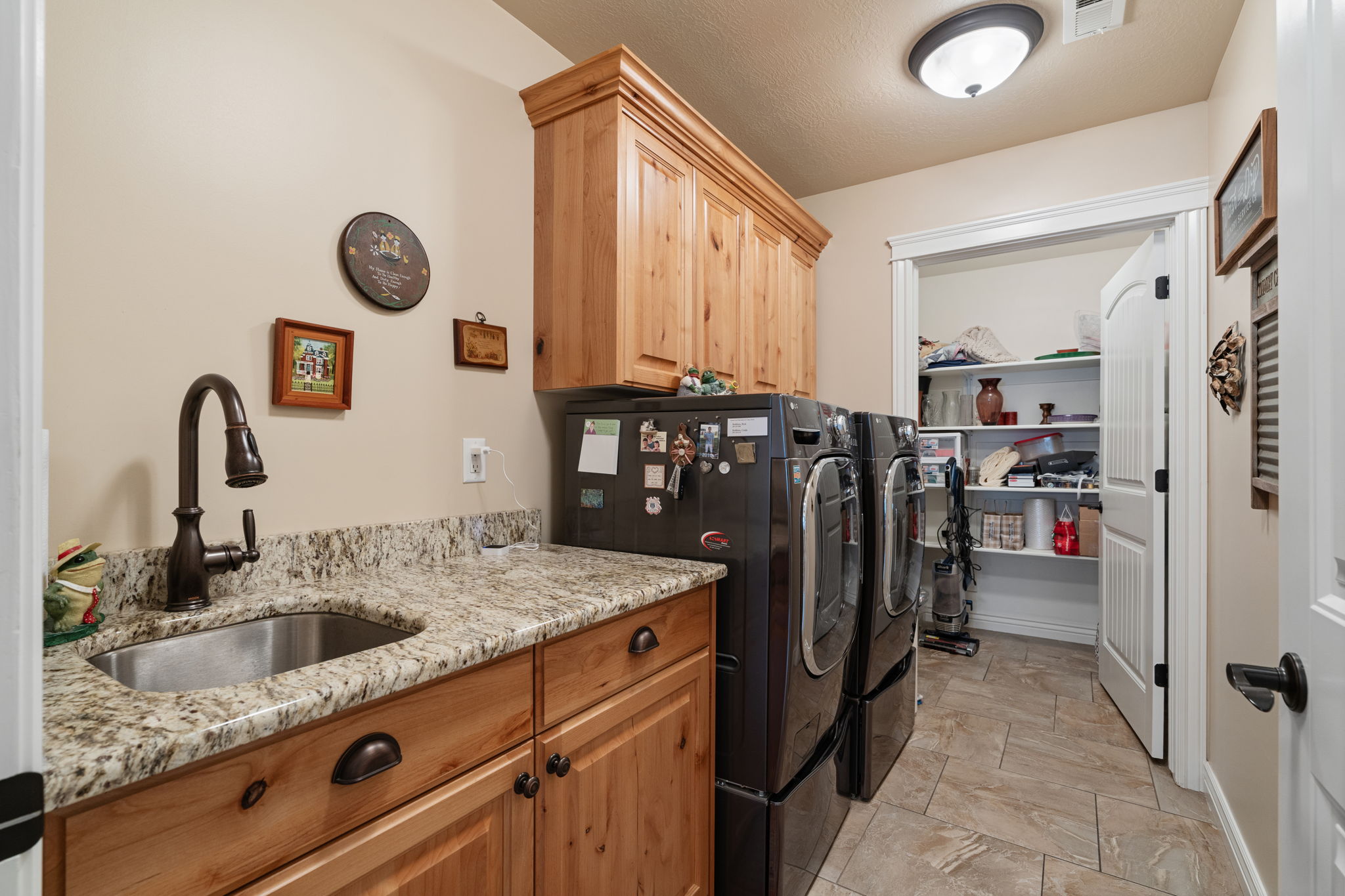 Laundry room featuring wood cabinetry, a stainless steel sink with a dark bronze faucet, and granite-style countertops