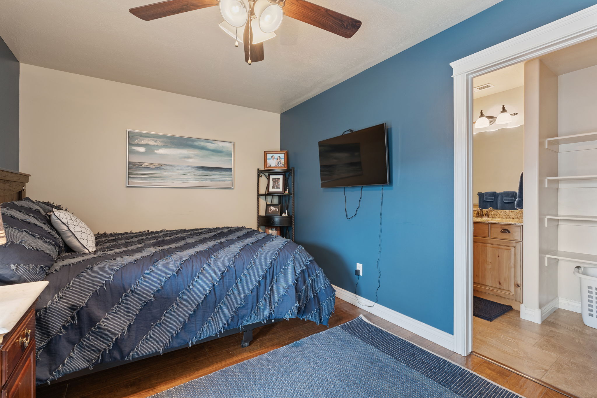 Bedroom featuring wood-finish flooring, a ceiling fan with integrated lighting, and a doorway leading to an additional space with a vanity and shelving