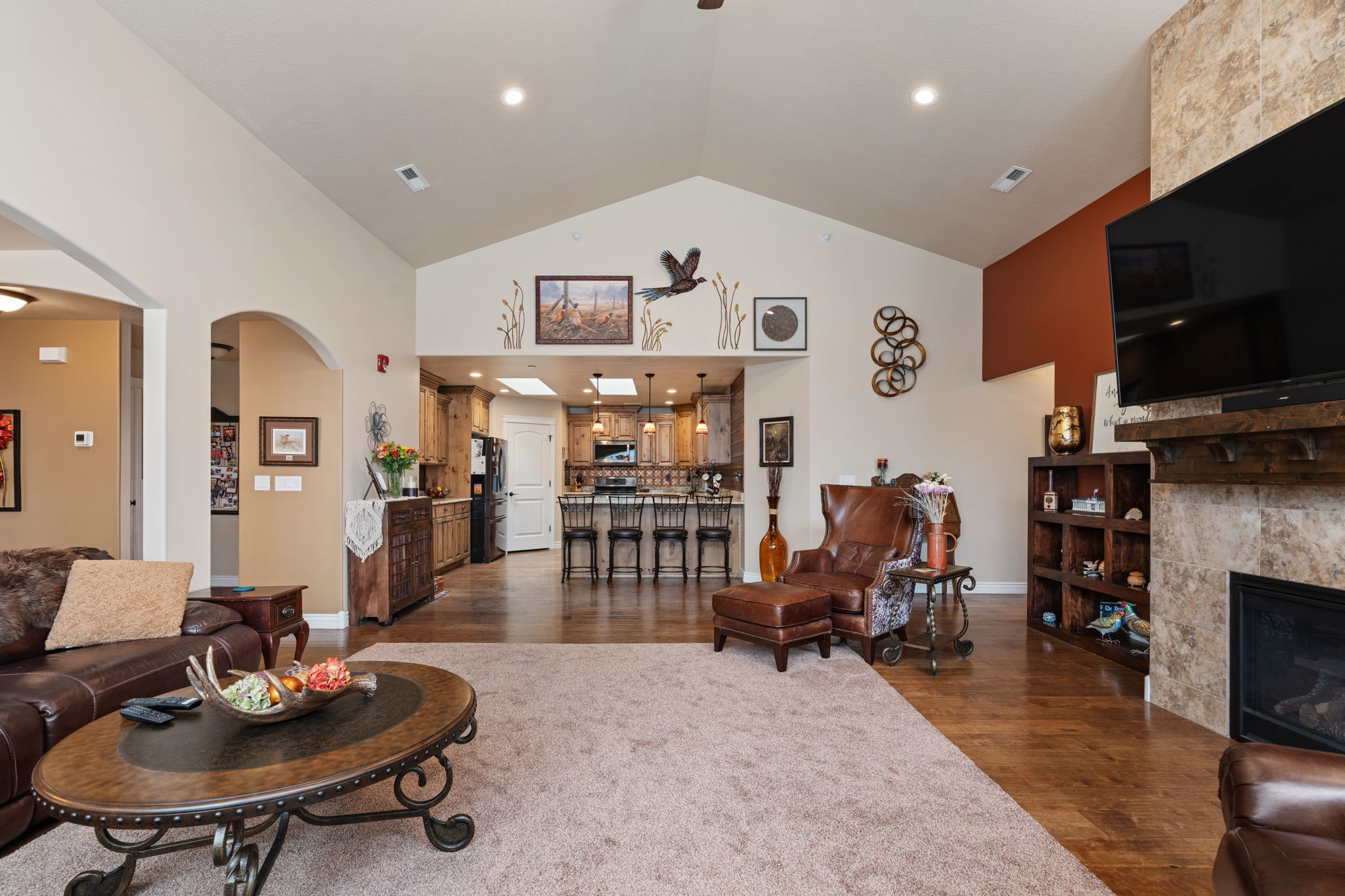 Spacious living area featuring vaulted ceilings, wood-finish flooring, and a stone-faced fireplace with a wood mantel