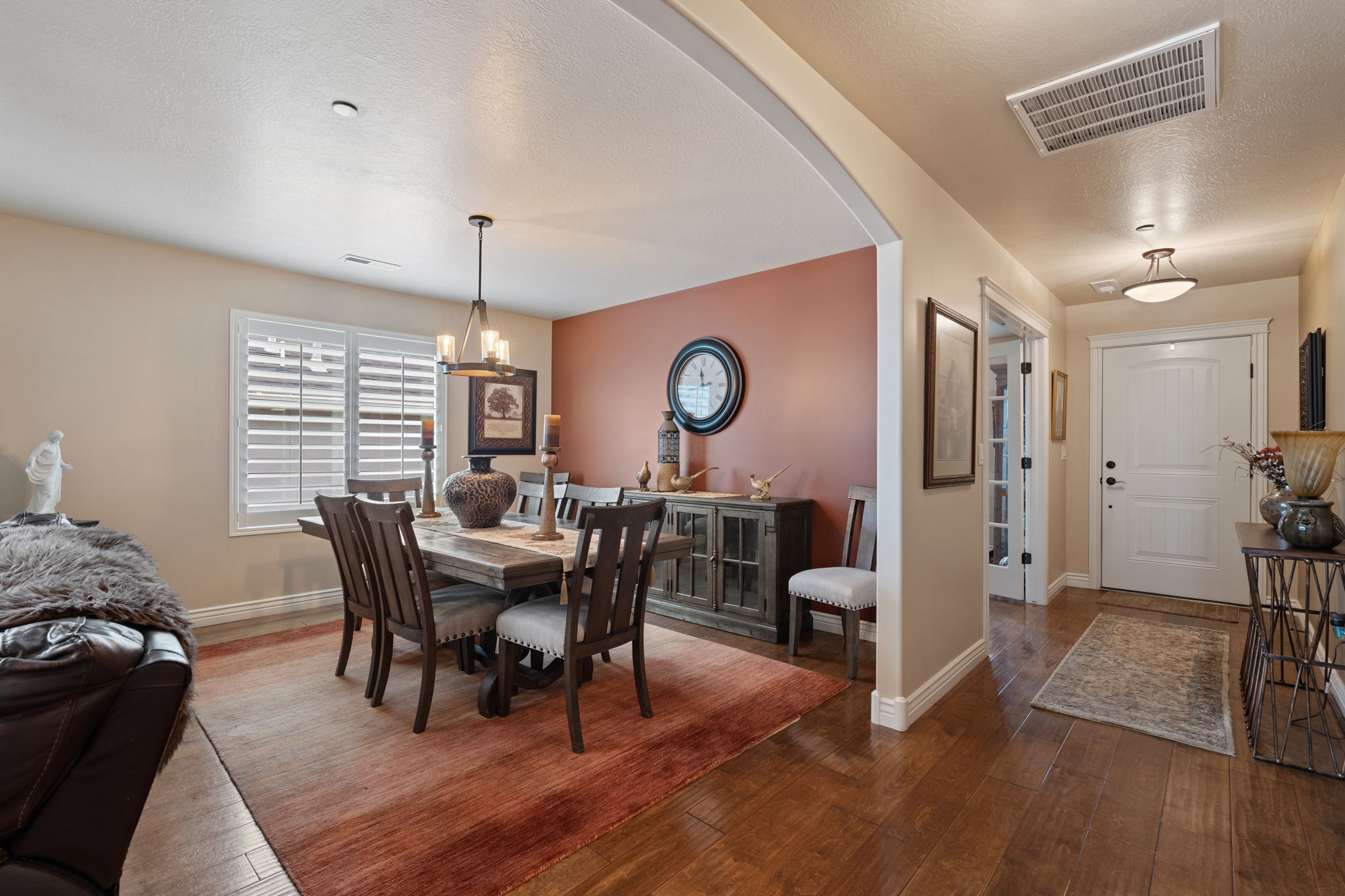 Open-concept dining area featuring a chandelier light fixture, large window with white plantation shutters, and wood-finish flooring