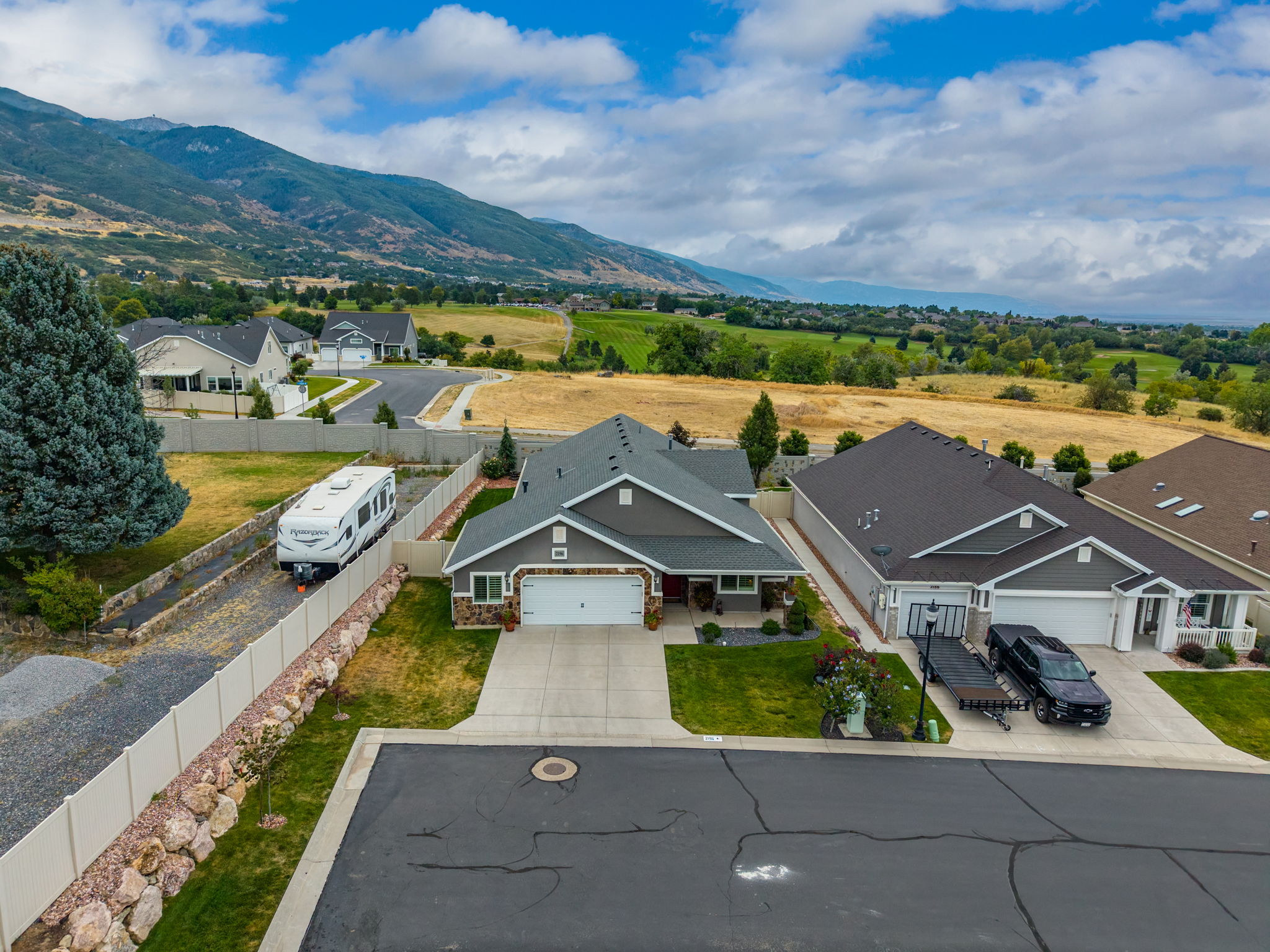 Contemporary ranch-style home featuring a two-car garage, manicured front lawn, stone veneer accents, an asphalt driveway, and a mountain backdrop
