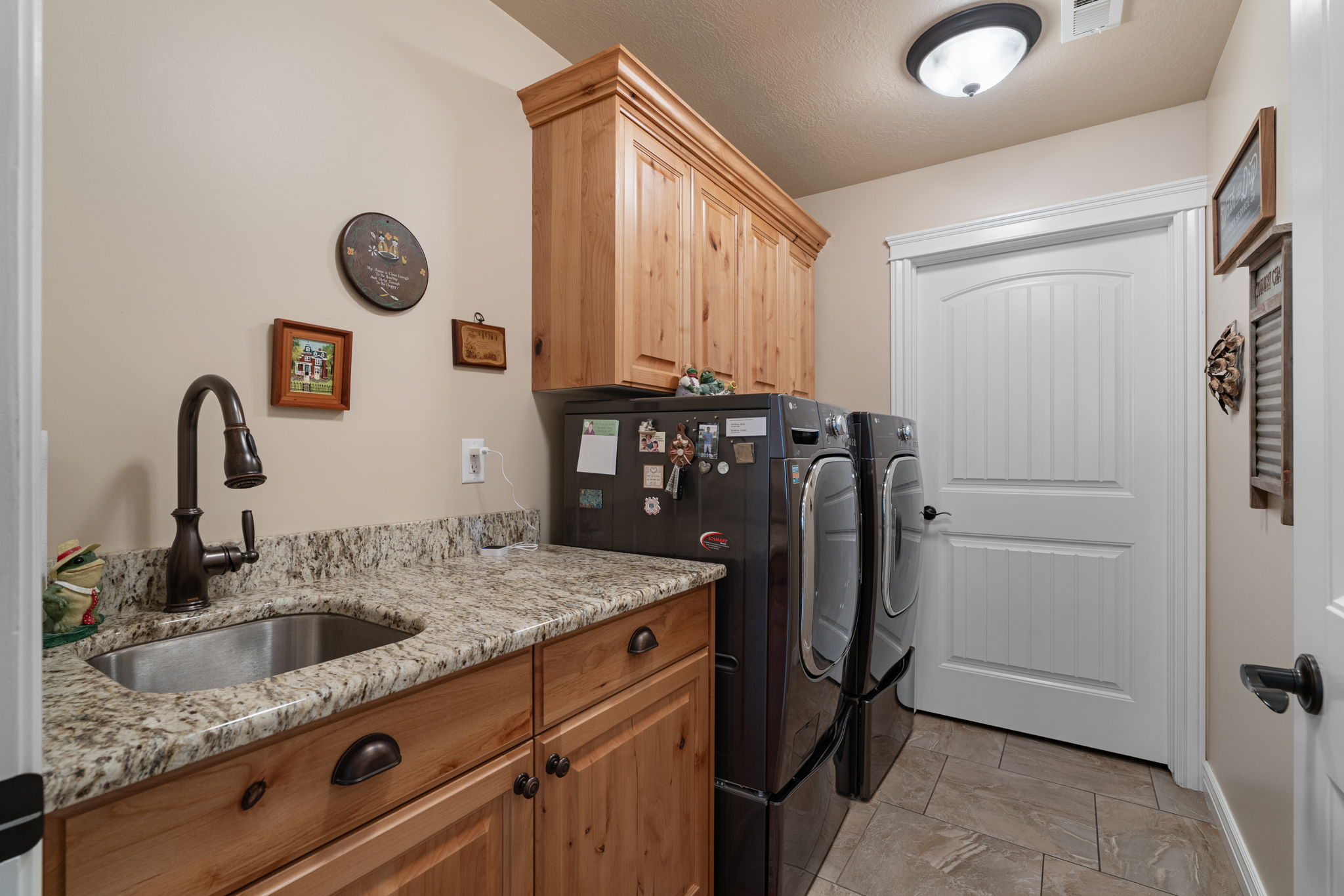 Laundry room featuring light wood cabinetry, a granite-finish countertop, and a stainless steel sink with a dark bronze faucet