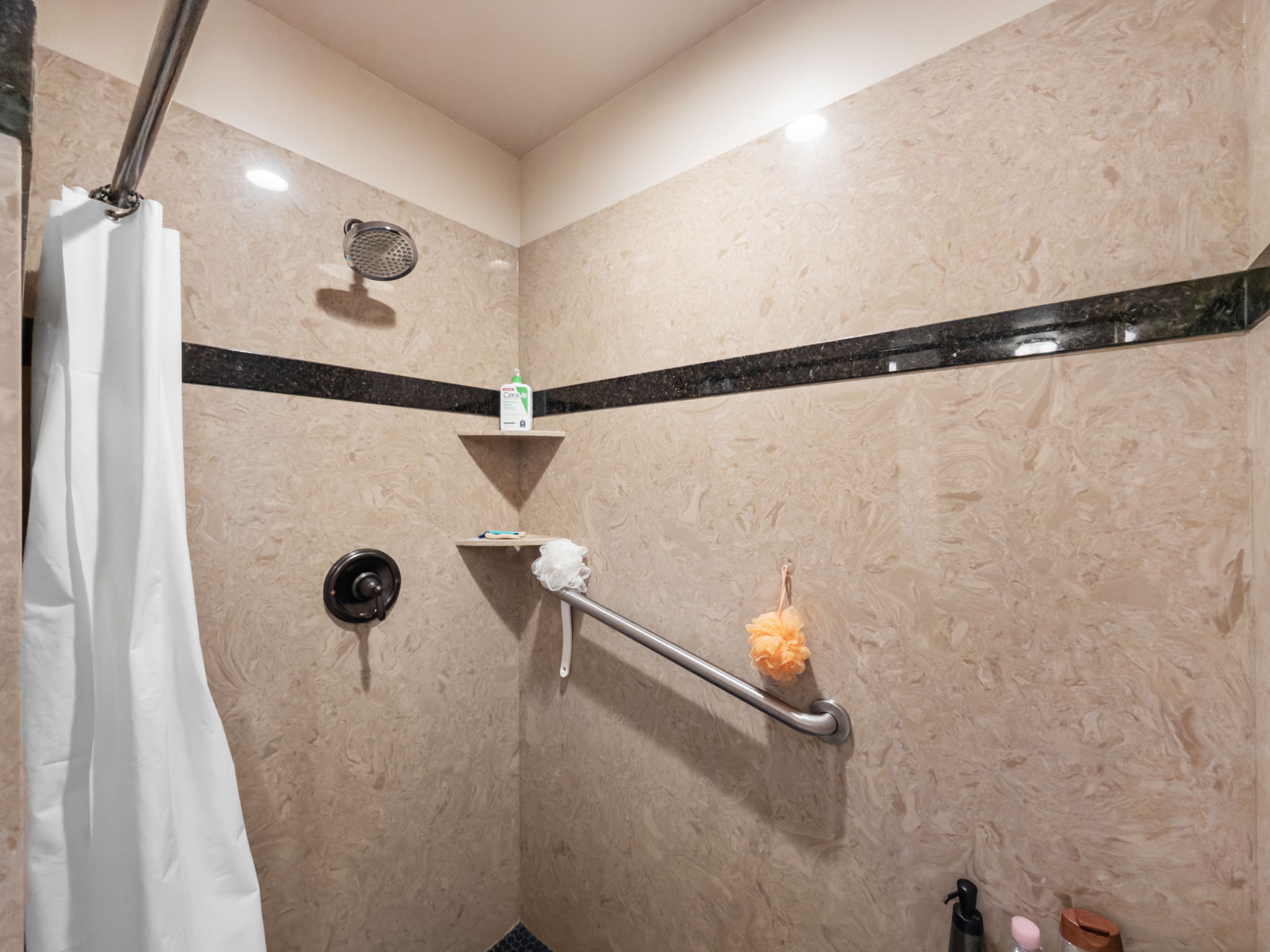 Shower enclosure featuring light-toned stone-look wall panels and a dark accent border