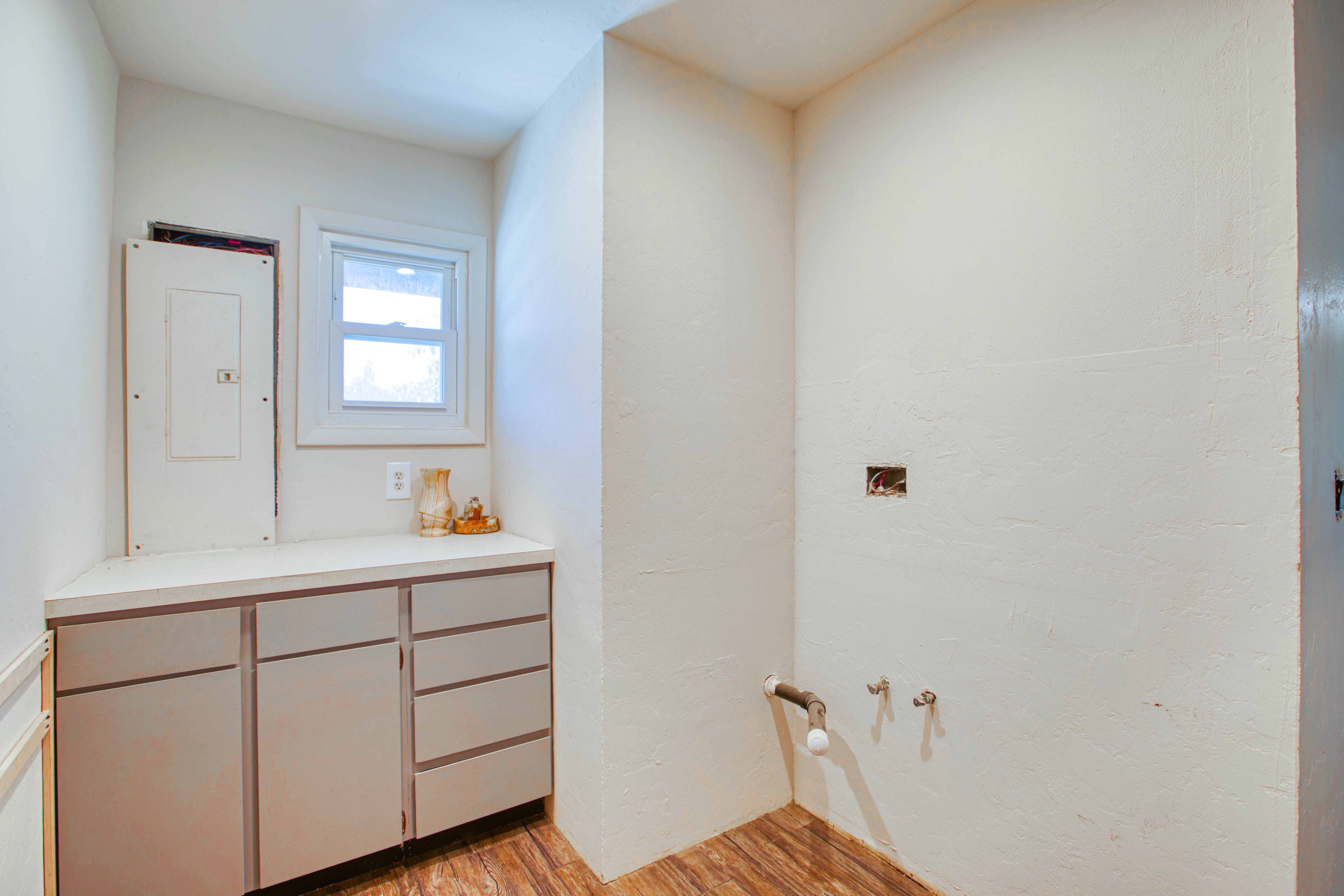 Utility area featuring wood-finish flooring, built-in cabinetry with a light-toned countertop, a single window, and visible plumbing hookups