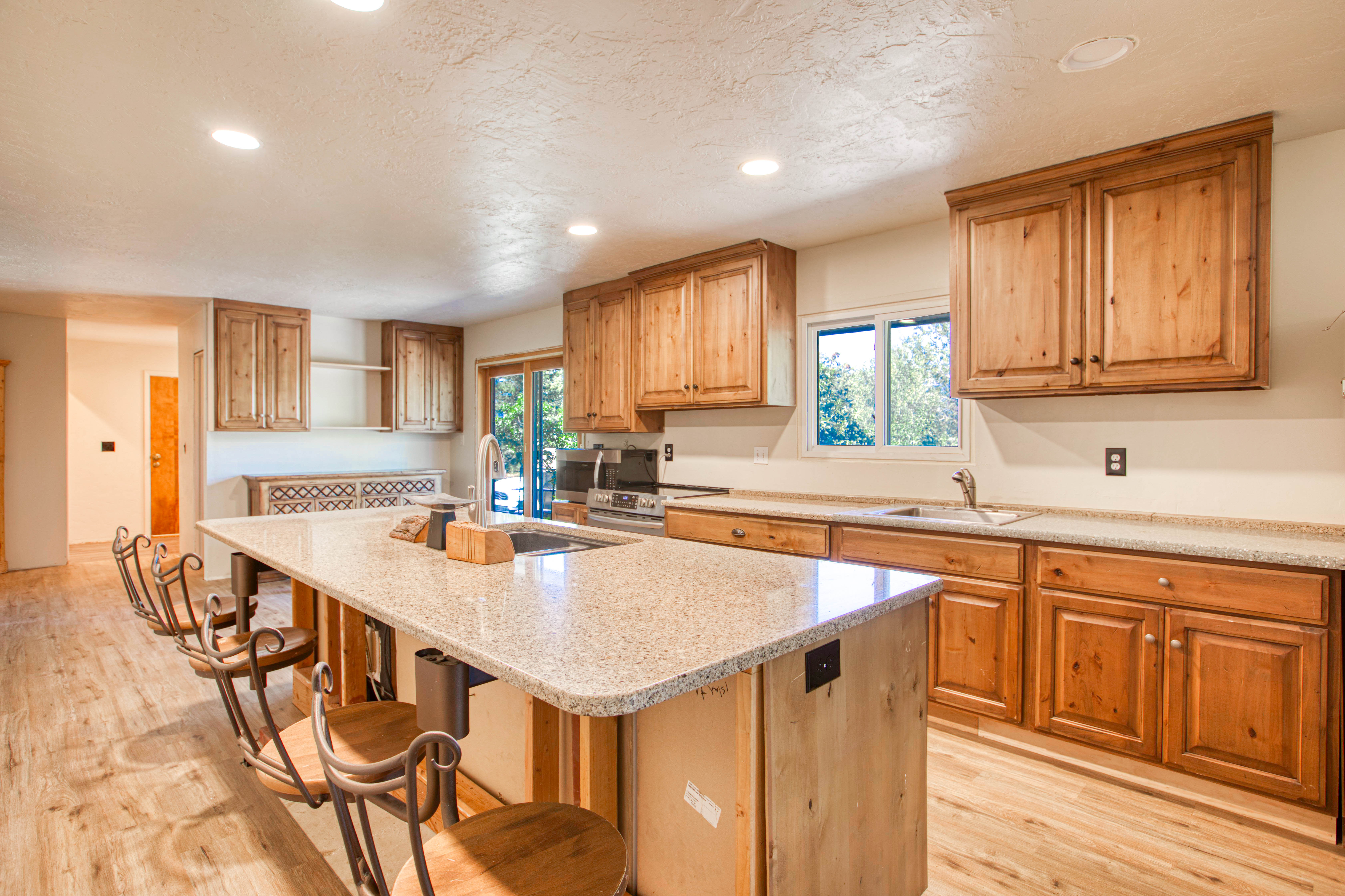 Kitchen featuring an expansive island with a stone-finish countertop, wood-finish flooring, recessed lighting, wood cabinetry, and a stainless steel sink