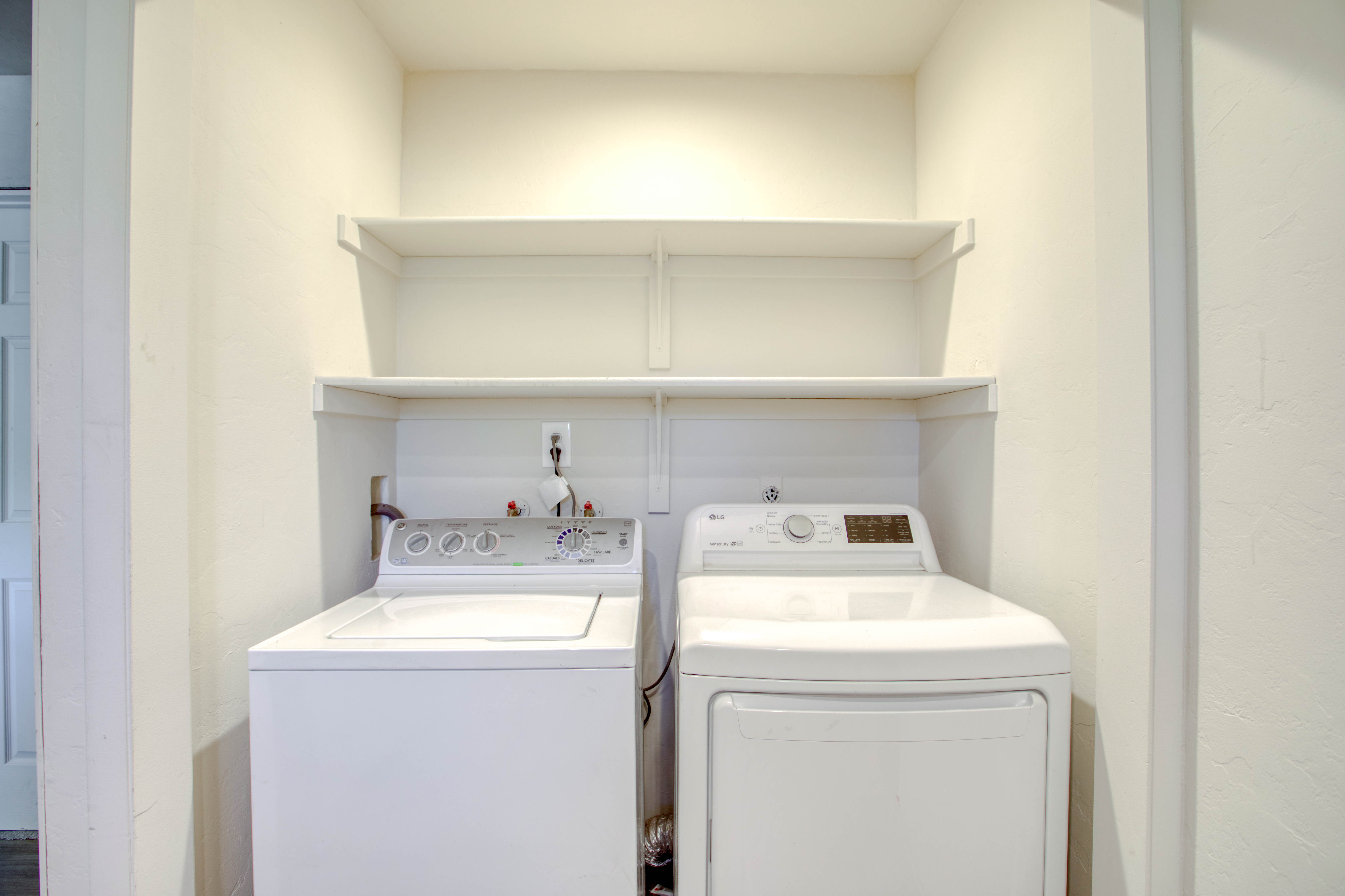 Dedicated laundry area featuring a top-load washing machine, front-load dryer, and integrated wall shelving