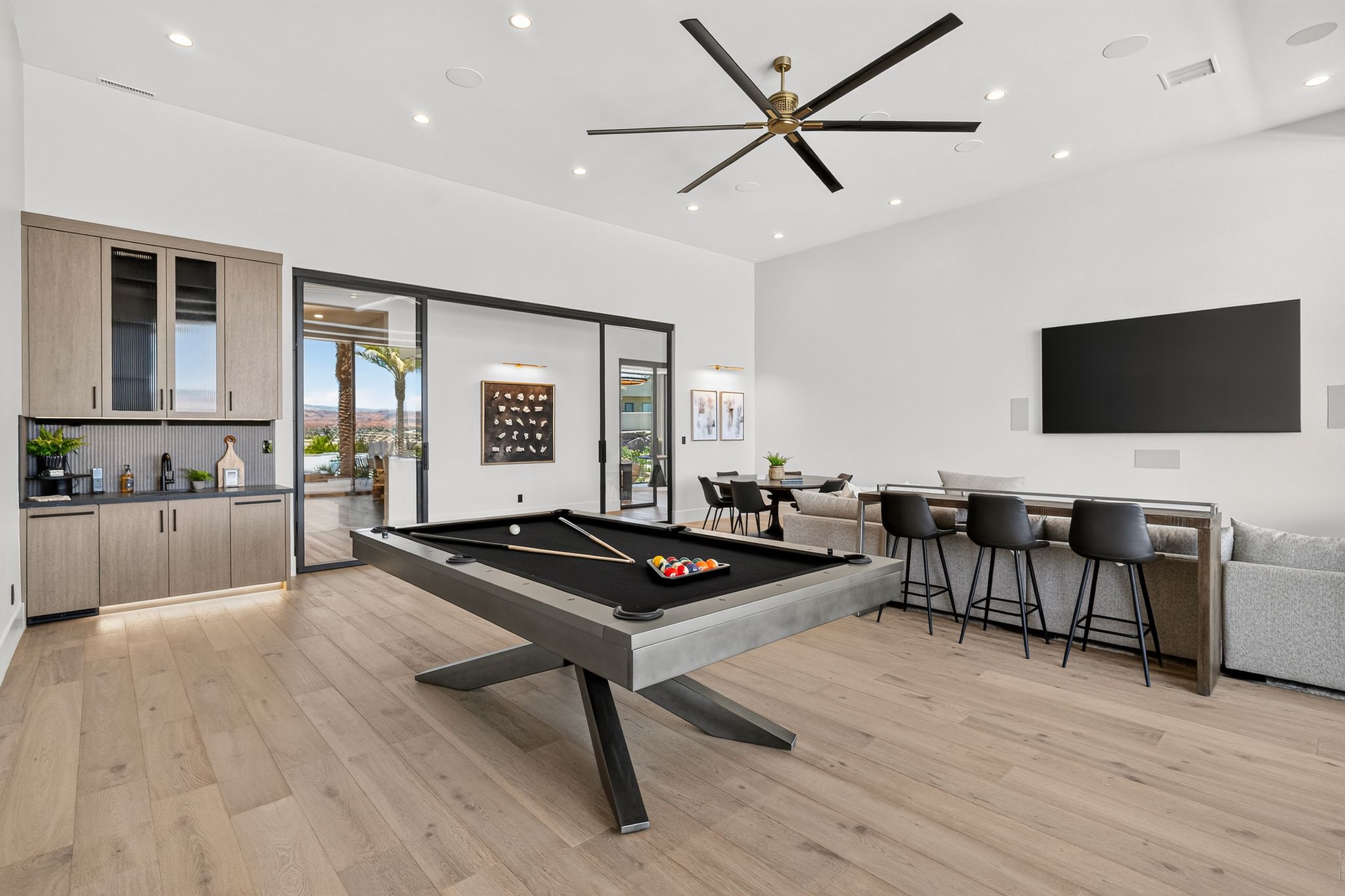 Wood-finish flooring throughout, featuring a built-in wet bar with cabinet storage, recessed lighting, and a large ceiling fan
