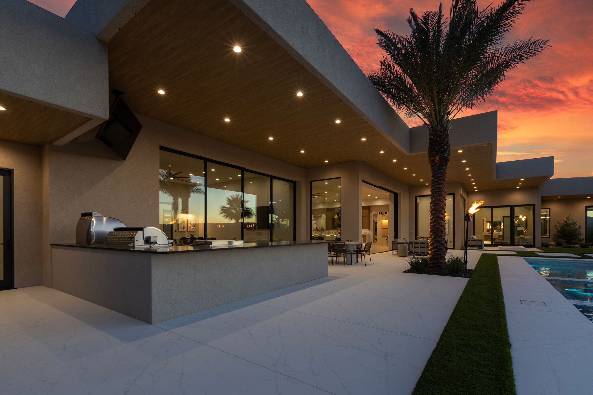 Expansive outdoor living area featuring a built-in barbecue station with stainless steel appliances, a large swimming pool, and mature palm trees