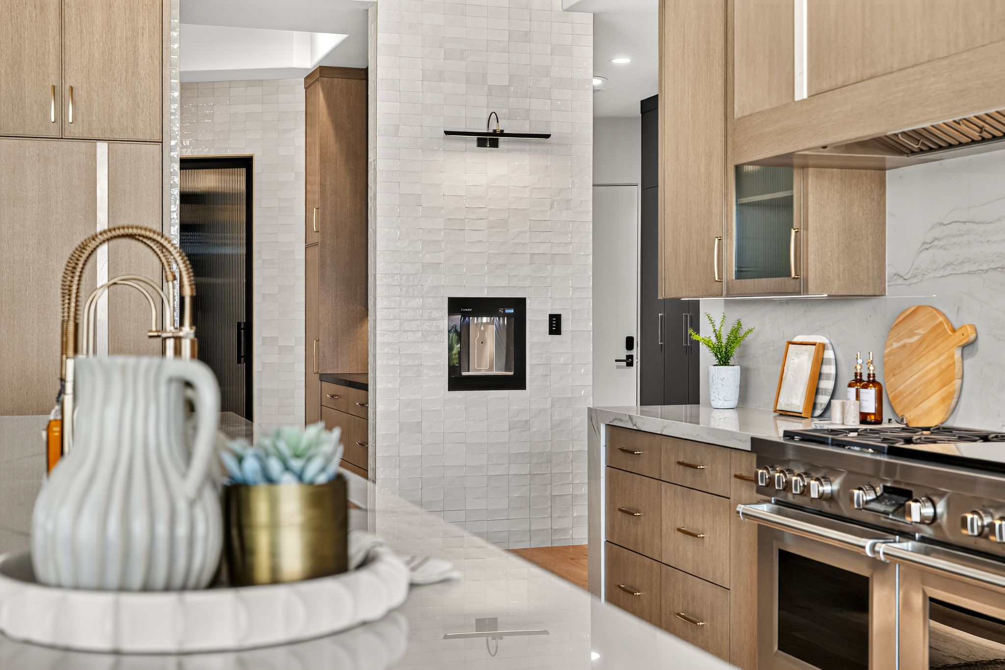 Modern kitchen featuring integrated stainless steel appliances, light wood-finish cabinetry, substantial countertops, a tiled backsplash, and an integrated beverage dispenser