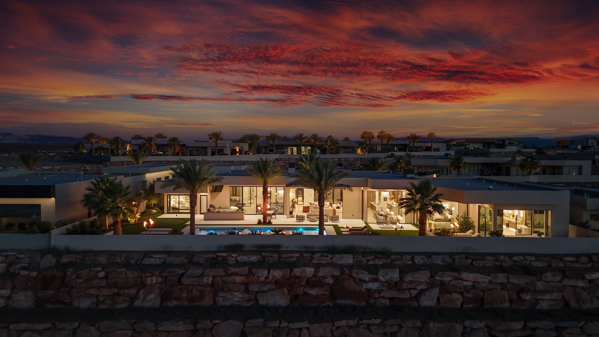 Contemporary exterior featuring a private swimming pool, integrated landscaping, multiple patio areas, and a retaining wall constructed from natural stone