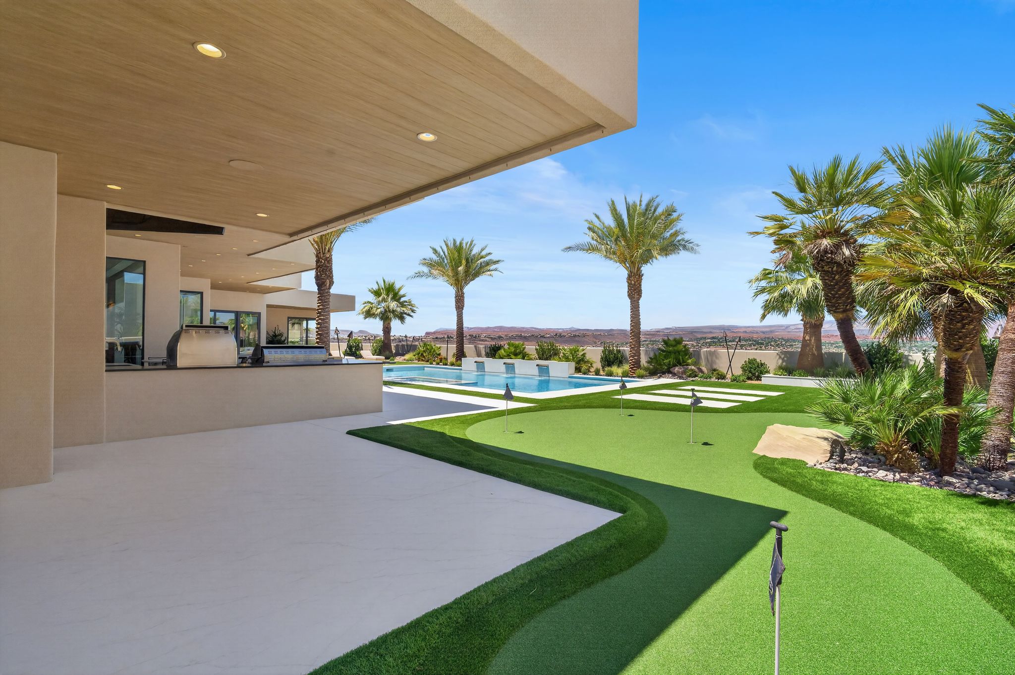 Covered patio with integrated outdoor kitchen, artificial turf putting green, and a swimming pool with water features