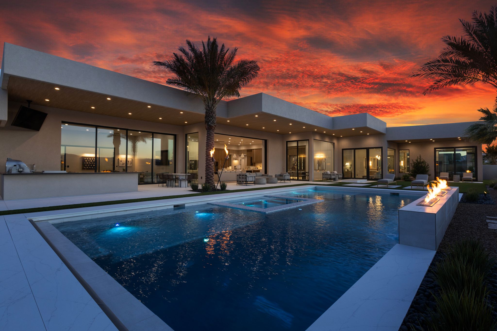 Contemporary exterior featuring a large swimming pool with integrated spa and underwater lighting, an integrated fire feature, an outdoor kitchen with built-in appliances, and expansive glass sliding doors