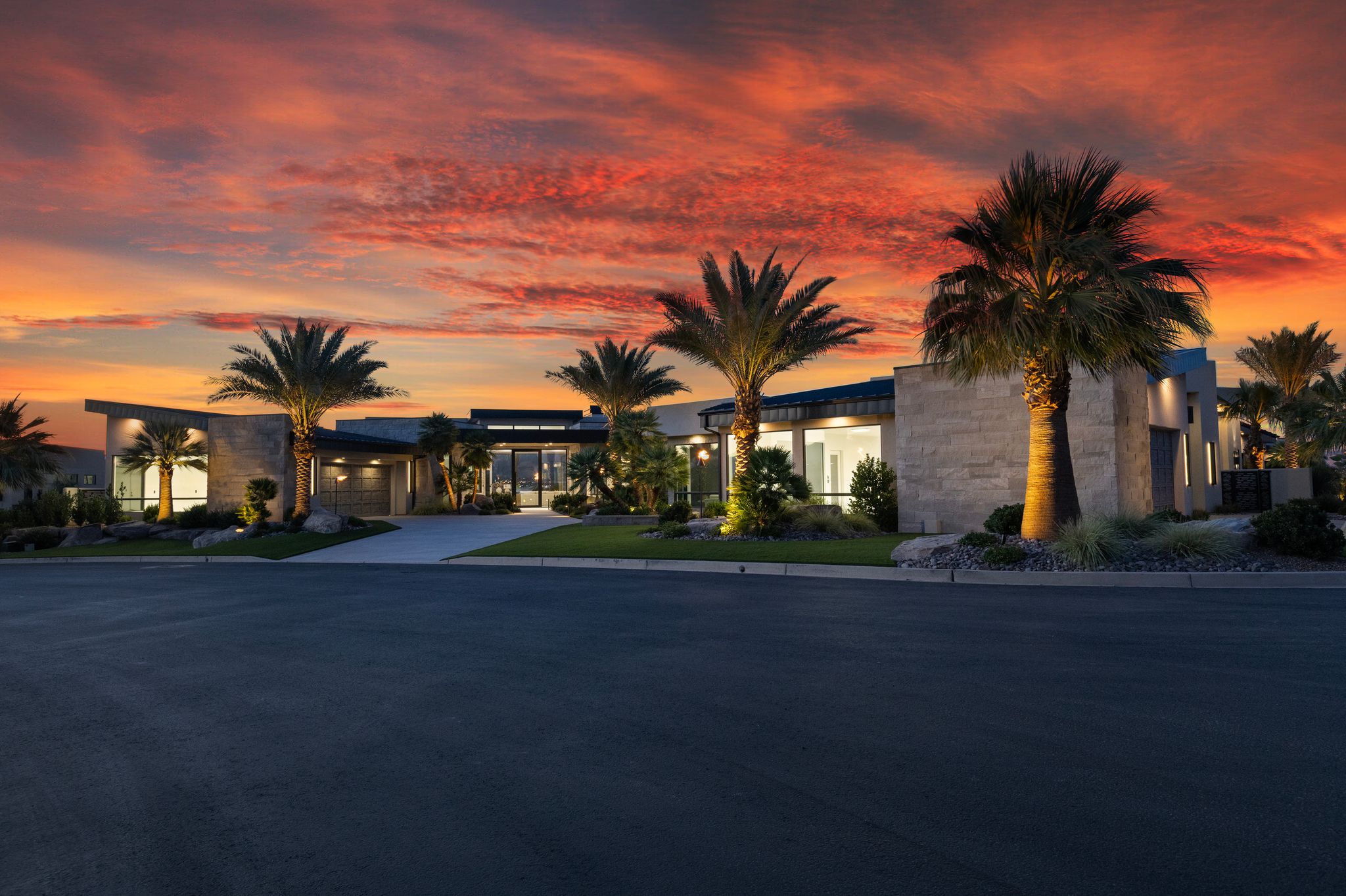 Modern architectural exterior featuring stone facade accents, extensive landscaping with palm trees, and integrated exterior lighting