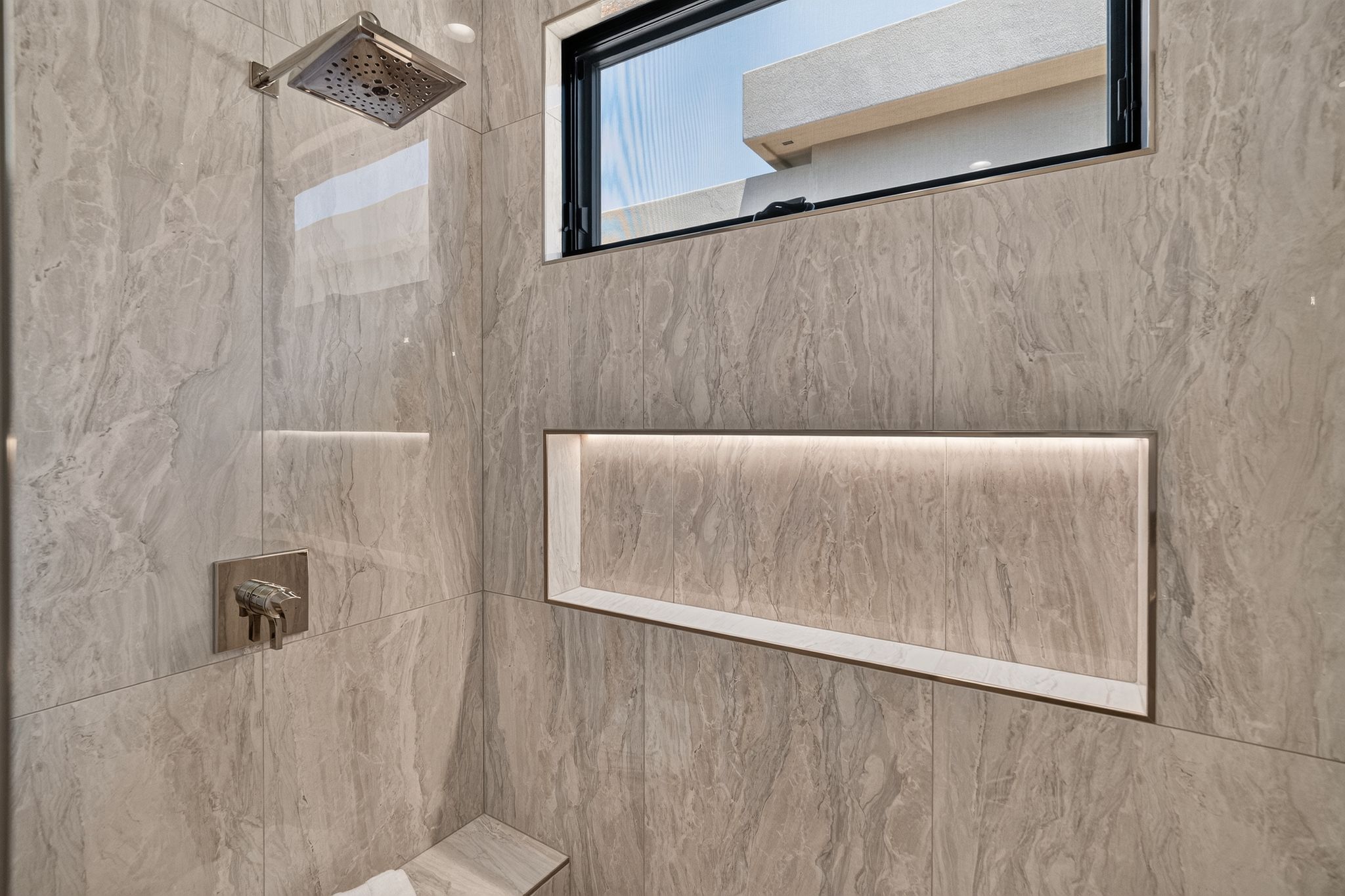 Shower enclosure featuring large format stone-look tiles and a built-in recessed niche with accent lighting