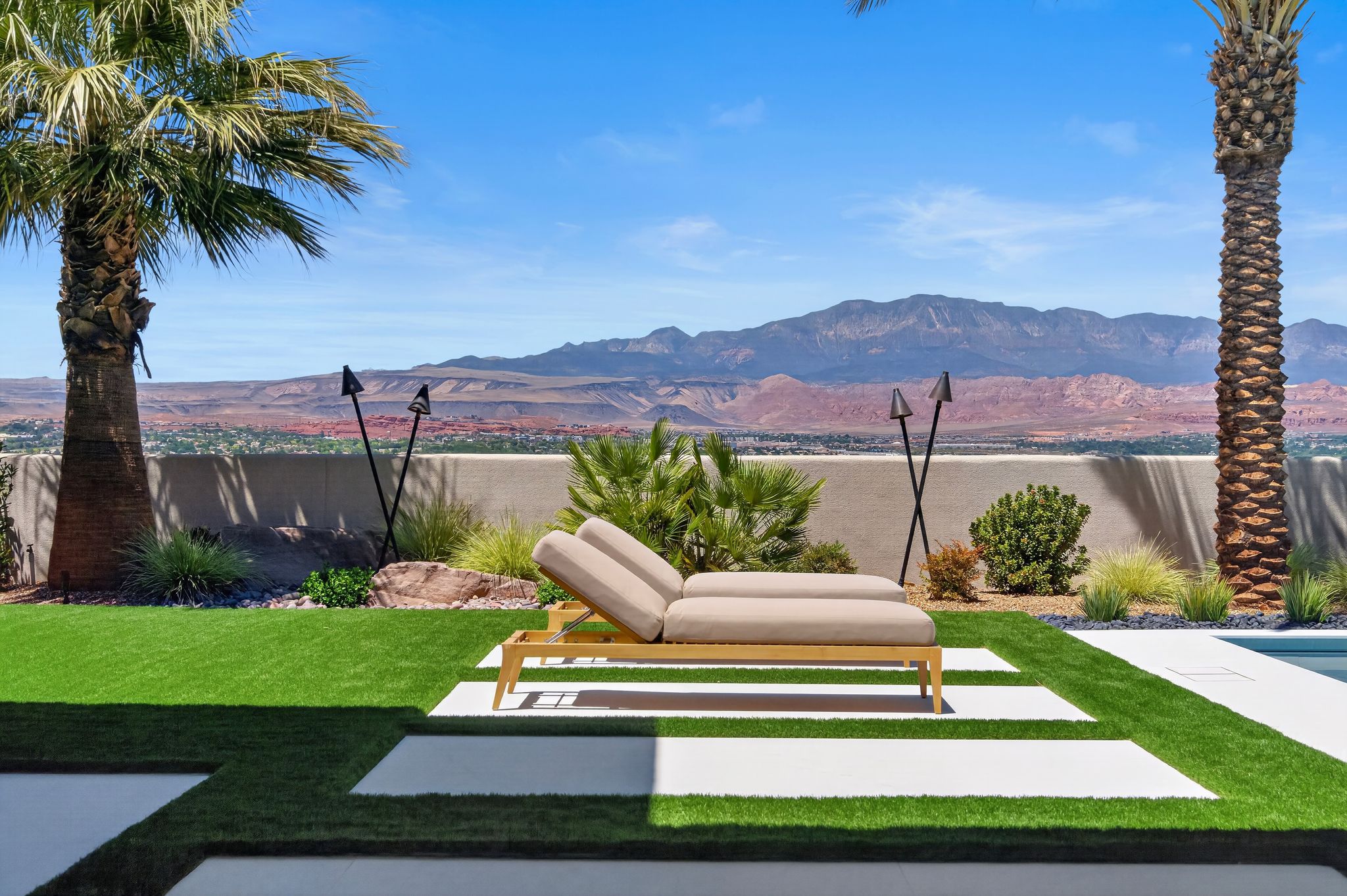 Outdoor living space featuring artificial turf, large format concrete pavers, mature palm trees, and a concrete perimeter wall