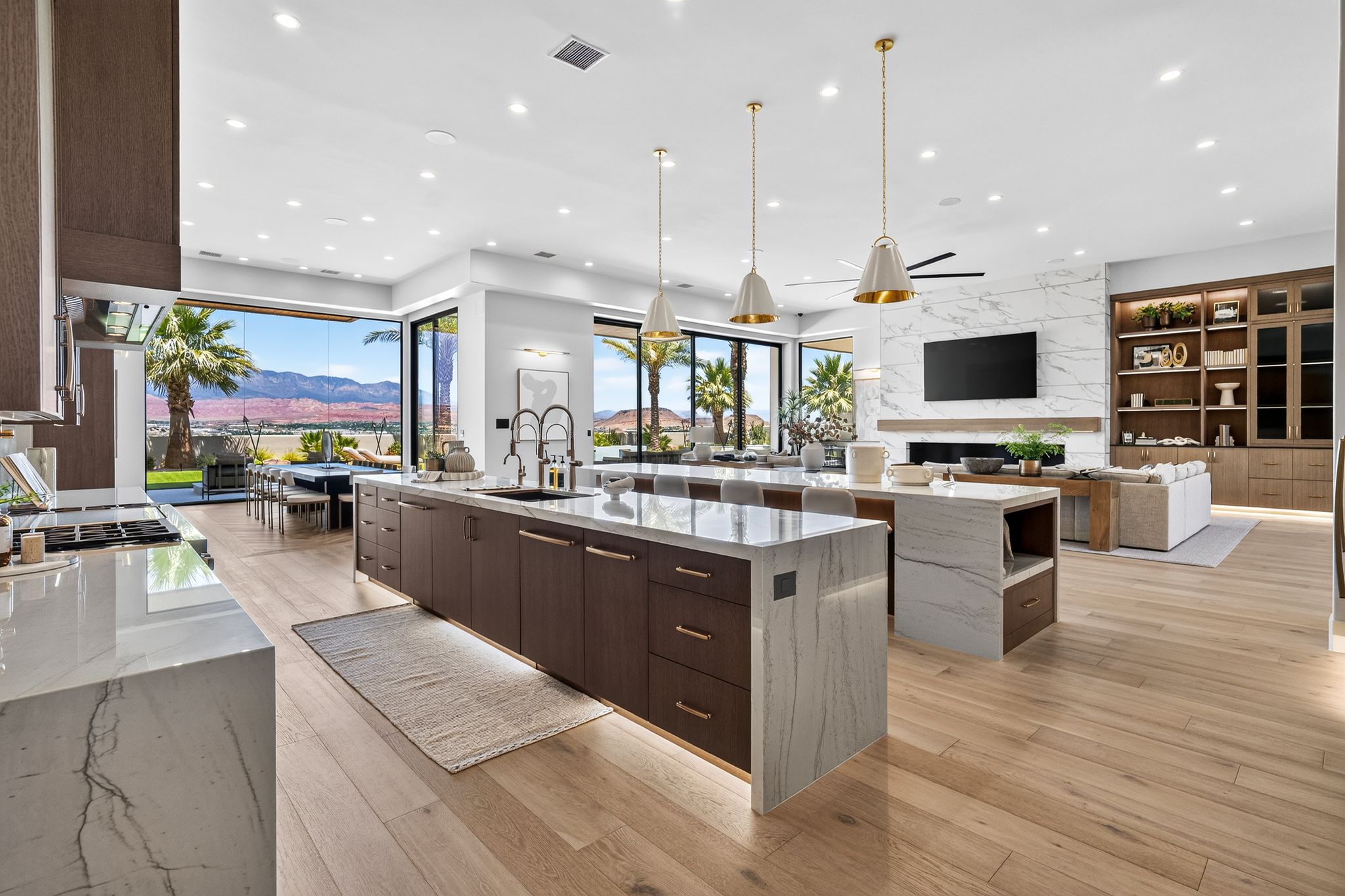 Spacious open-concept living area featuring a gourmet kitchen with waterfall island, wood-finish flooring, a contemporary fireplace with a large format tile surround, and full-height built-in shelving