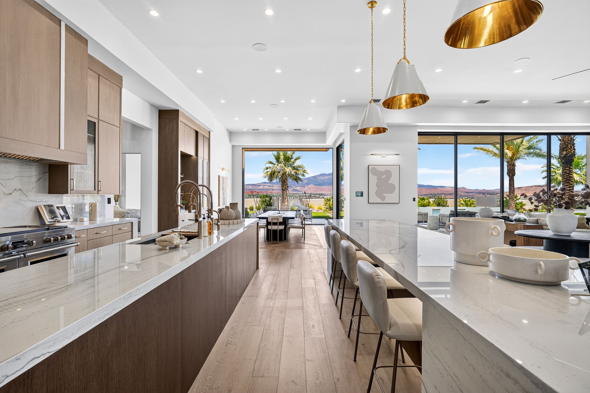 Expansive kitchen featuring a large central island with seating, additional island with sink, wood-finish flooring, and light-toned cabinetry