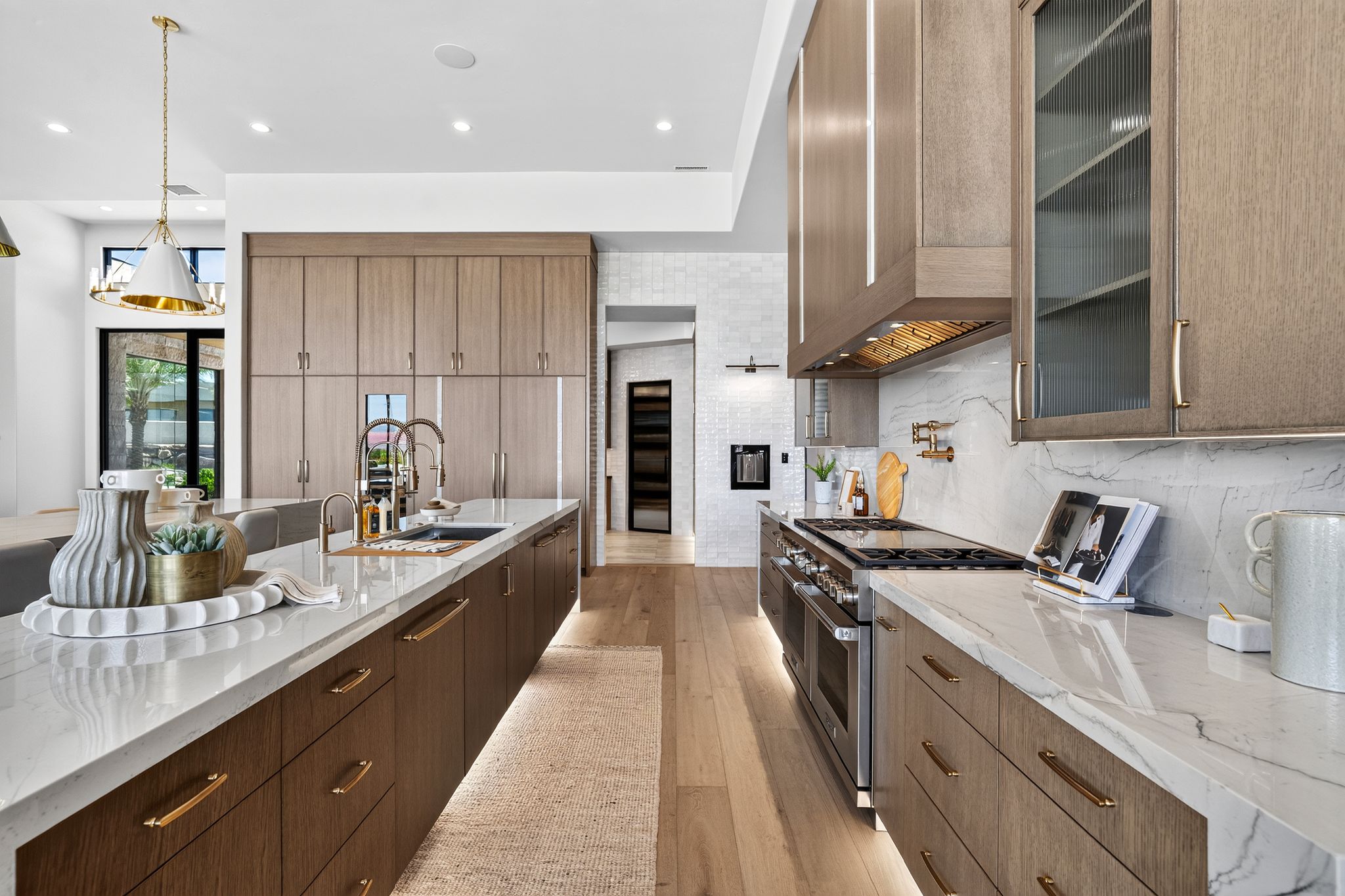 Gourmet kitchen featuring a large central island with integrated sink, two-tone cabinetry with under-cabinet lighting, stainless steel appliances, and wood-finish flooring
